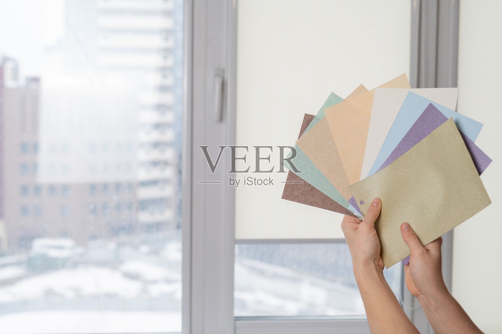 女人在窗户背景前拿着卷帘布样本。照片摄影图片