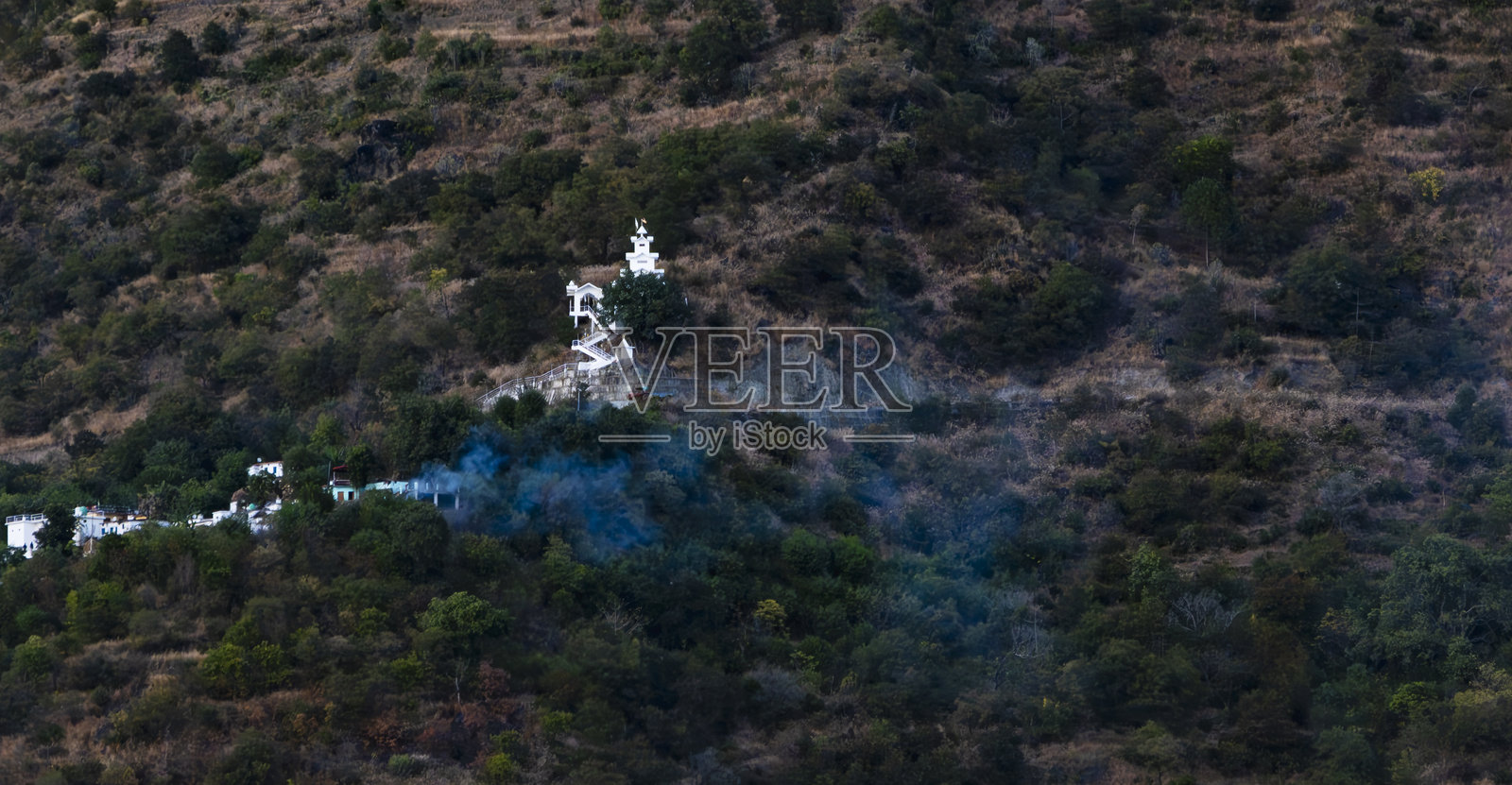 一座白色寺庙坐落在山丘上，周围有台阶和郁郁葱葱的植被。附近房屋冒出的烟雾为特赫里湖增添了宁静的氛围。照片摄影图片