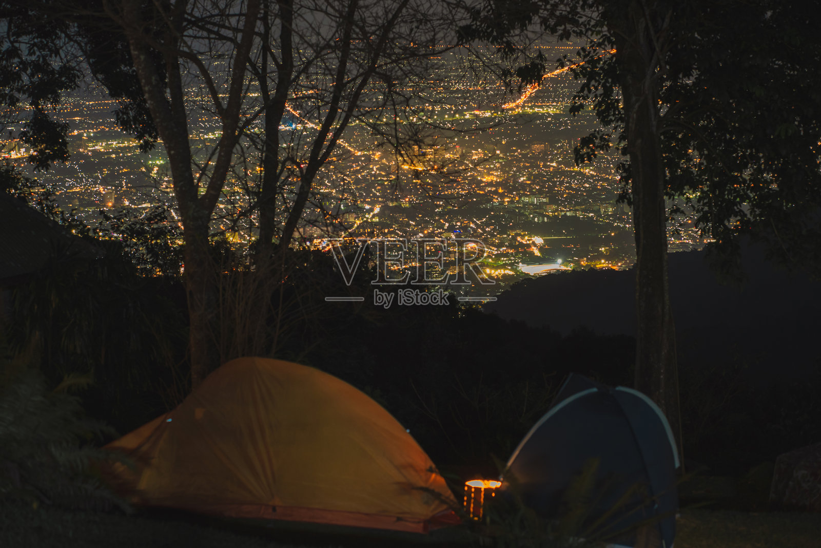 山上和城市背景下，男人在帐篷旁放松的风景与旅行概念照片摄影图片