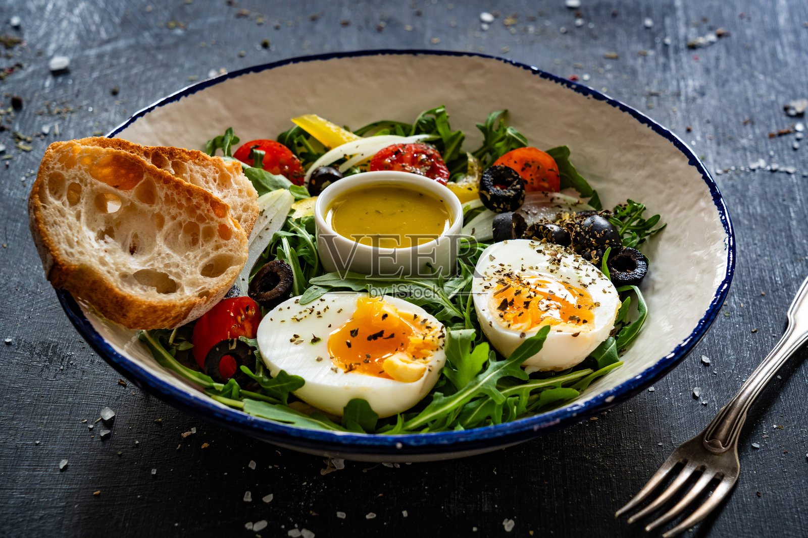 新鲜的绿色沙拉，配有蔬菜、煮鸡蛋和黑色桌子上的油醋汁照片摄影图片