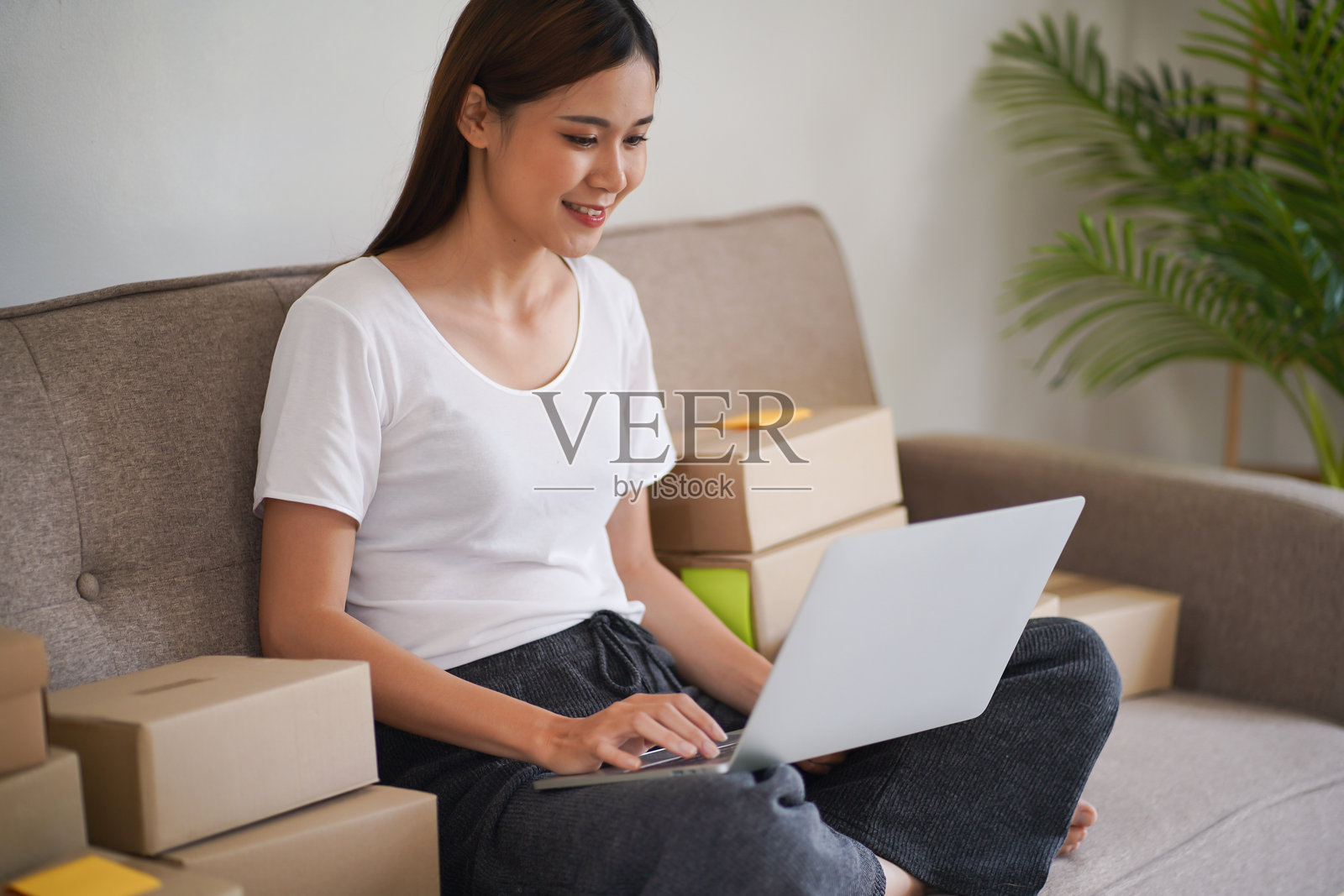 在家工作的亚洲女性准备包裹寄送箱，进行在线购物的发货。年轻的初创小企业主在家处理在线订单。照片摄影图片