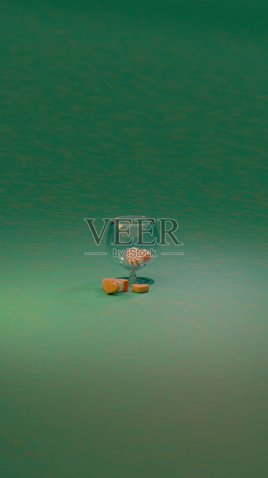 红白相间的心形糖果静静地放在一只空透明玻璃旁边，背景是一片简单的绿色表面。照片摄影图片