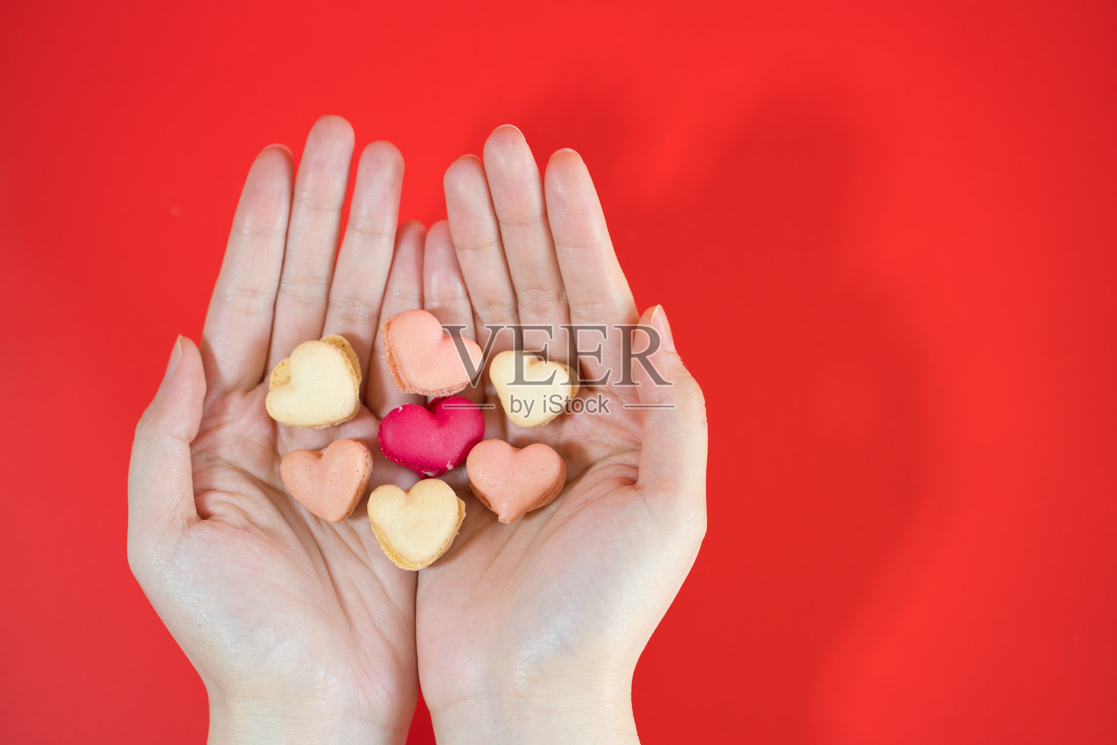 红色背景上手中摆放的心形马卡龙平铺图照片摄影图片
