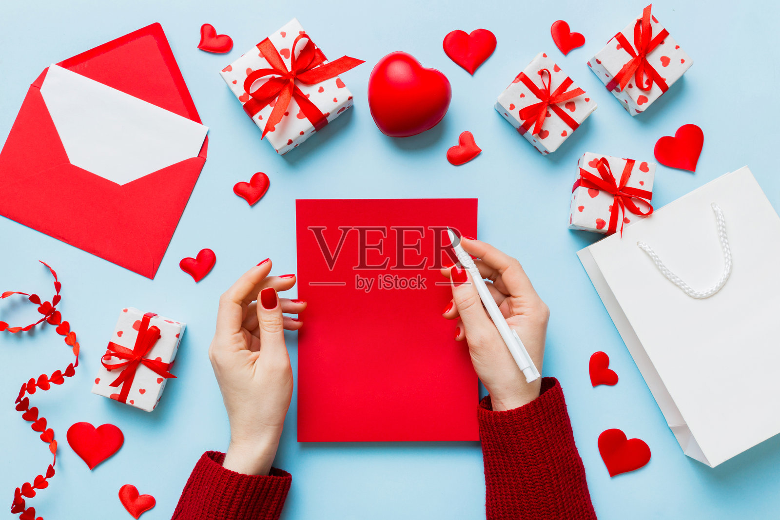 从上方拍摄的情人节装饰照片，女性手握着信件和信封，旁边有小礼物盒和心形装饰，背景为单色柔和色调，留有空白空间。照片摄影图片
