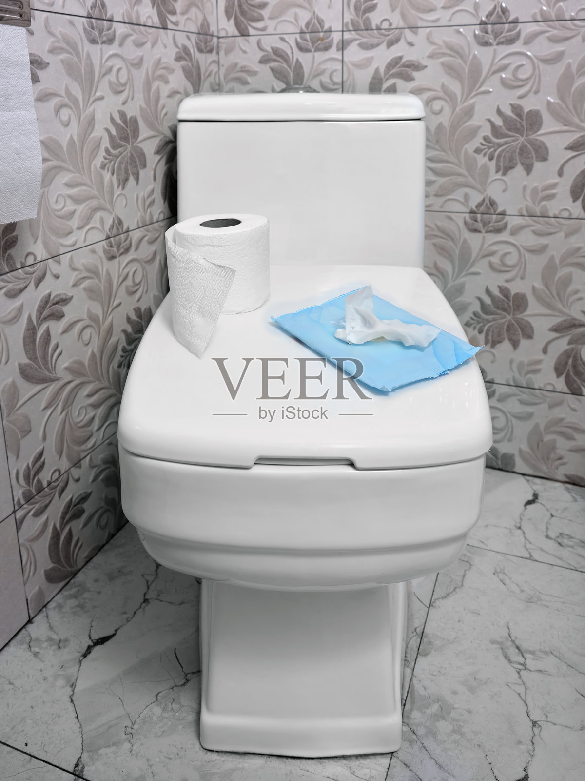 公寓浴室内，卫生间盖上放着一卷卫生纸和湿纸巾的竖直图像。照片摄影图片