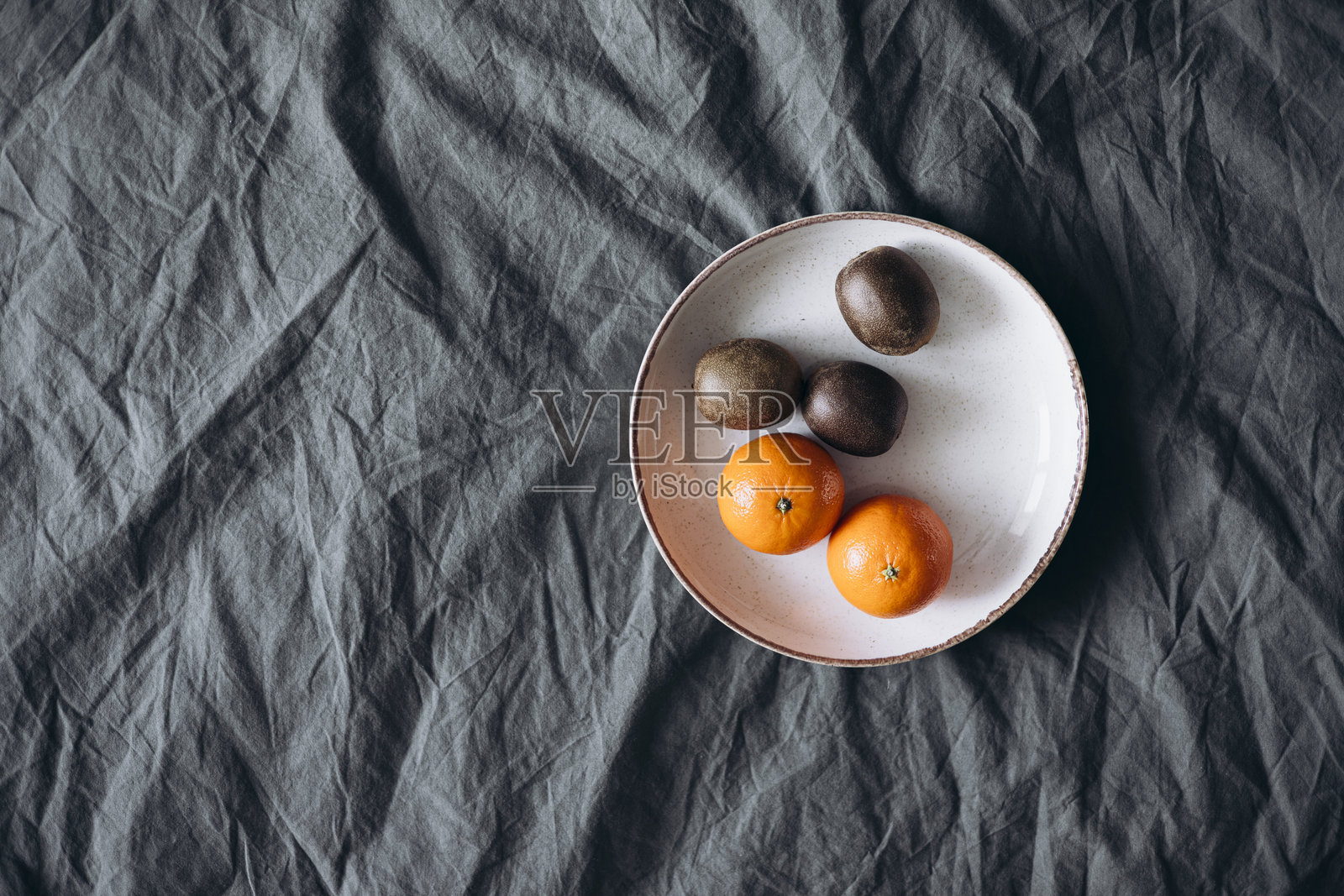 床上的盘子里放着新鲜的猕猴桃和橘子，俯视图。照片摄影图片