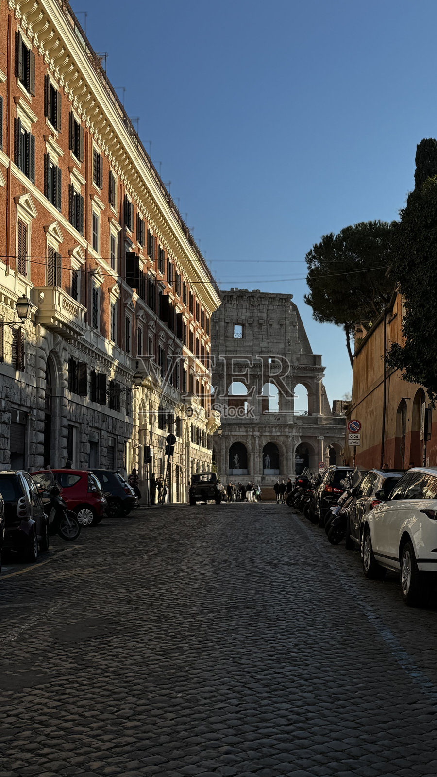罗马的鹅卵石街道，远眺古老的斗兽场和历史建筑，映衬在明亮的蓝天之下。照片摄影图片