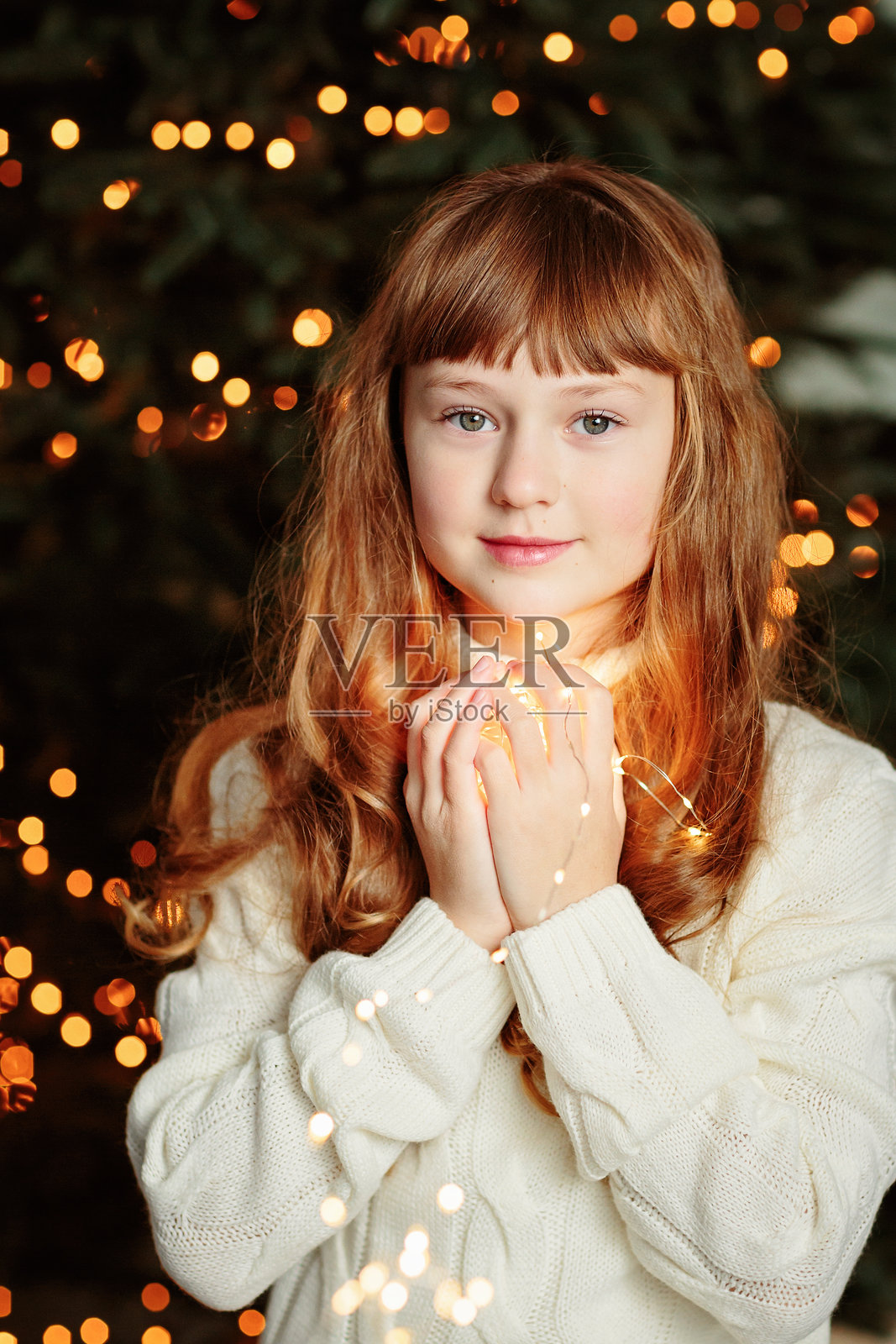 快乐的小女孩坐在圣诞树旁，身边有彩带。照片摄影图片