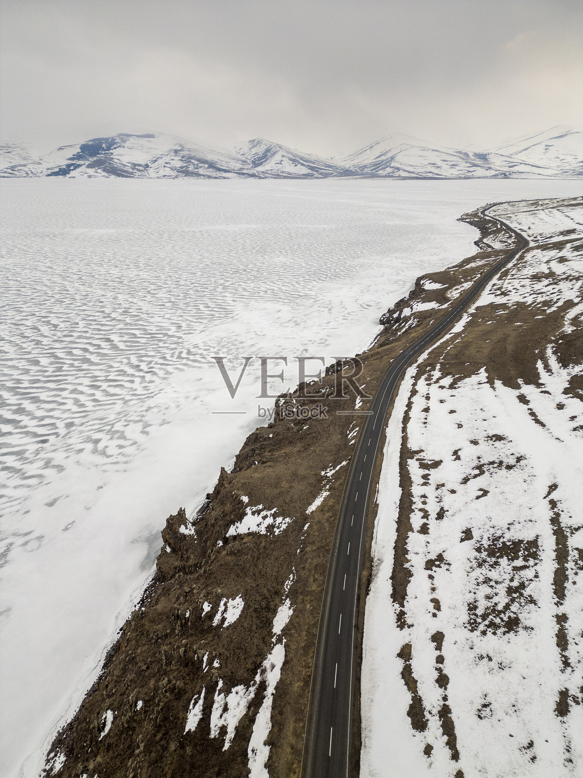 冰冻的湖面和延伸至远方的雪-covered道路，背景是山脉。照片摄影图片