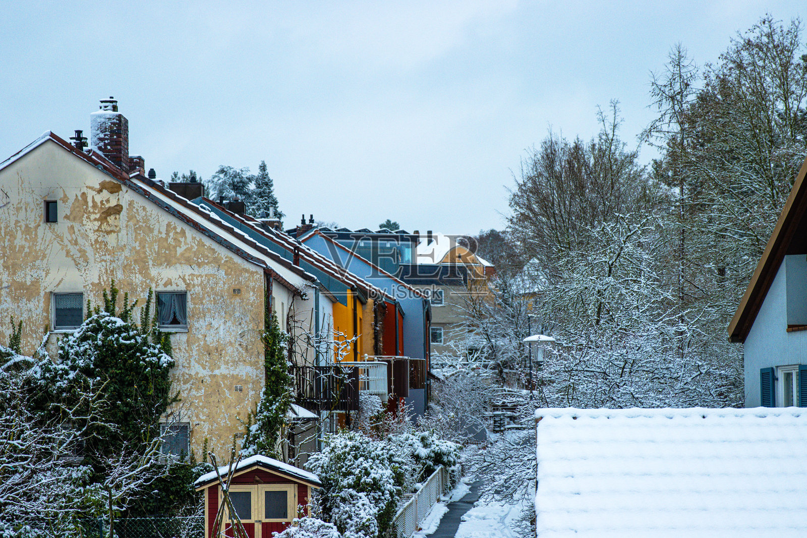 雪覆盖的住宅区，五彩斑斓的房屋和结霜的树木。郊区冬季风景，房屋、屋顶、树木上覆盖着新雪，天空阴云密布。留白空间照片摄影图片
