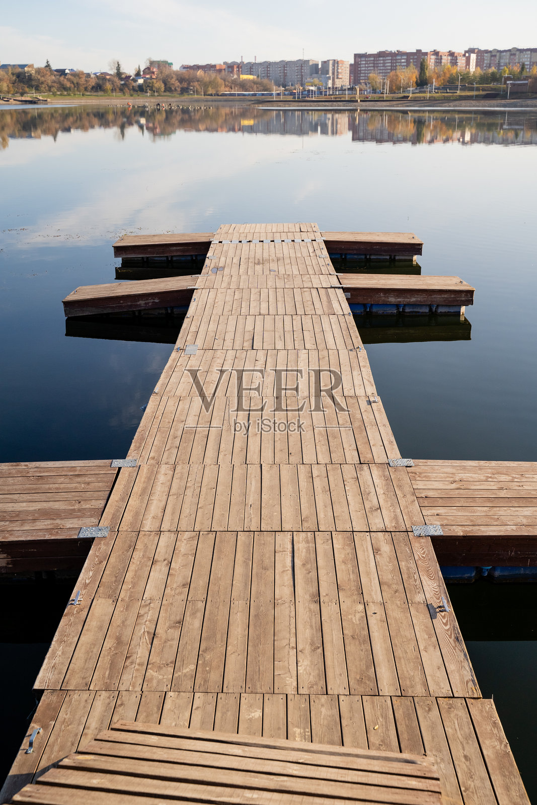 一座如画的木栈道优雅地延伸至宁静的湖泊，背景中一座生机勃勃的城市天际线巍然屹立，形成了自然与城市生活的美丽对比。照片摄影图片