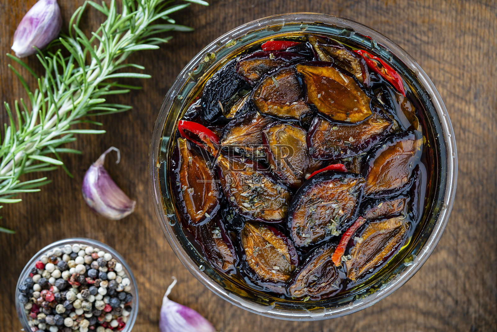 阳光晒干的梅子与大蒜、绿色迷迭香、红辣椒、橄榄油和香料放在木桌上的玻璃罐中。乡村风格，俯视图，特写。照片摄影图片