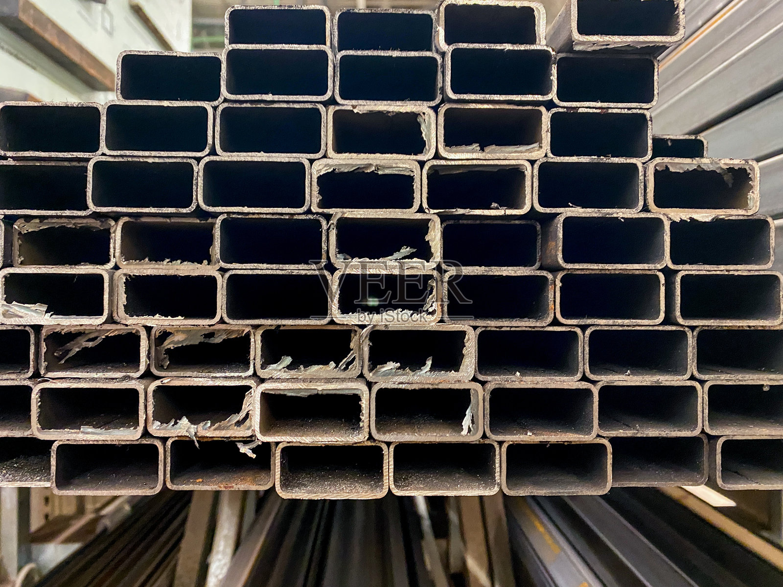 在一个宽敞的仓库里，有一堆高耸的金属管道，整齐地排列和堆叠在一起，展示了它们坚固的结构和耐用性。照片摄影图片