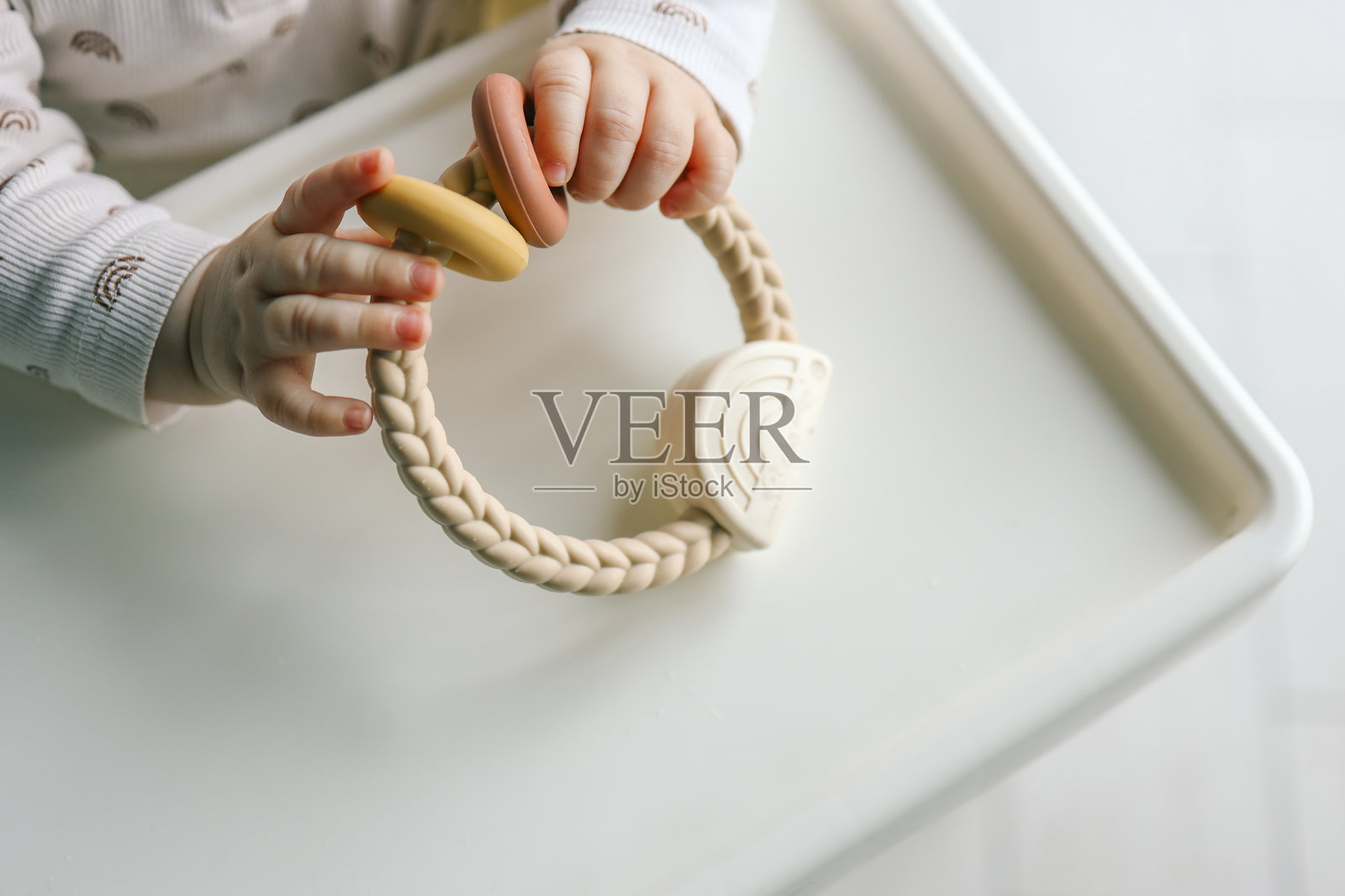 婴儿的小手握着一个极简主义的硅胶牙胶，带有编织手柄和柔和色彩的环。简单现代的设计，适合舒缓和感官游戏。照片摄影图片