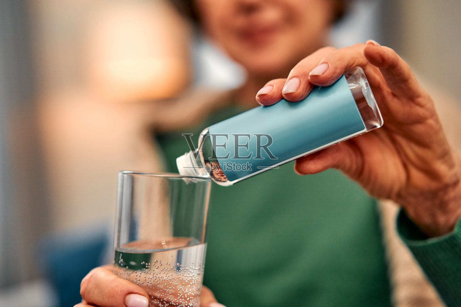特写照片：一位女性手持一杯水和一瓶药物，正在将它们倒入一个玻璃杯中。膳食补充剂，健康护理。照片摄影图片