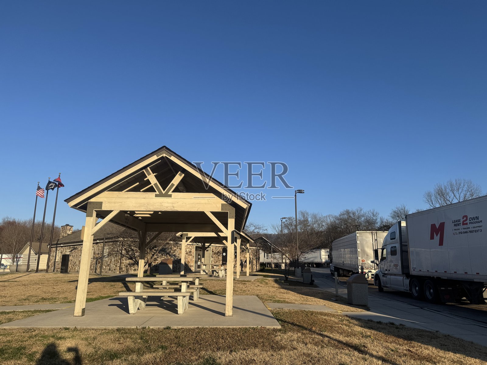 阳光明媚的下午，在靠近停车区的野餐棚下，视野中有卡车和旗帜。照片摄影图片