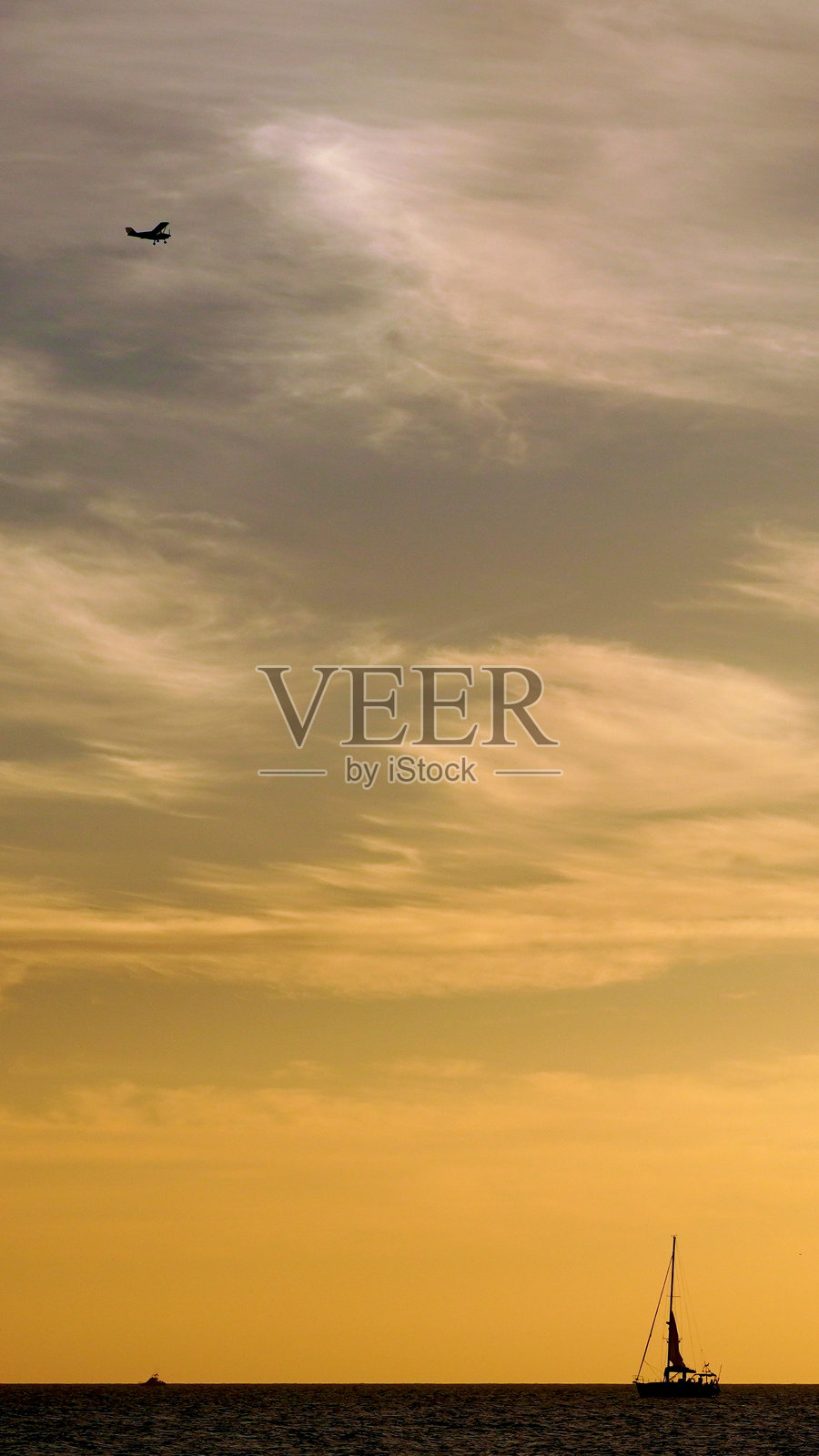 在加那利群岛，日落时分，一艘帆船正在航行，一架小飞机在空中飞行。照片摄影图片