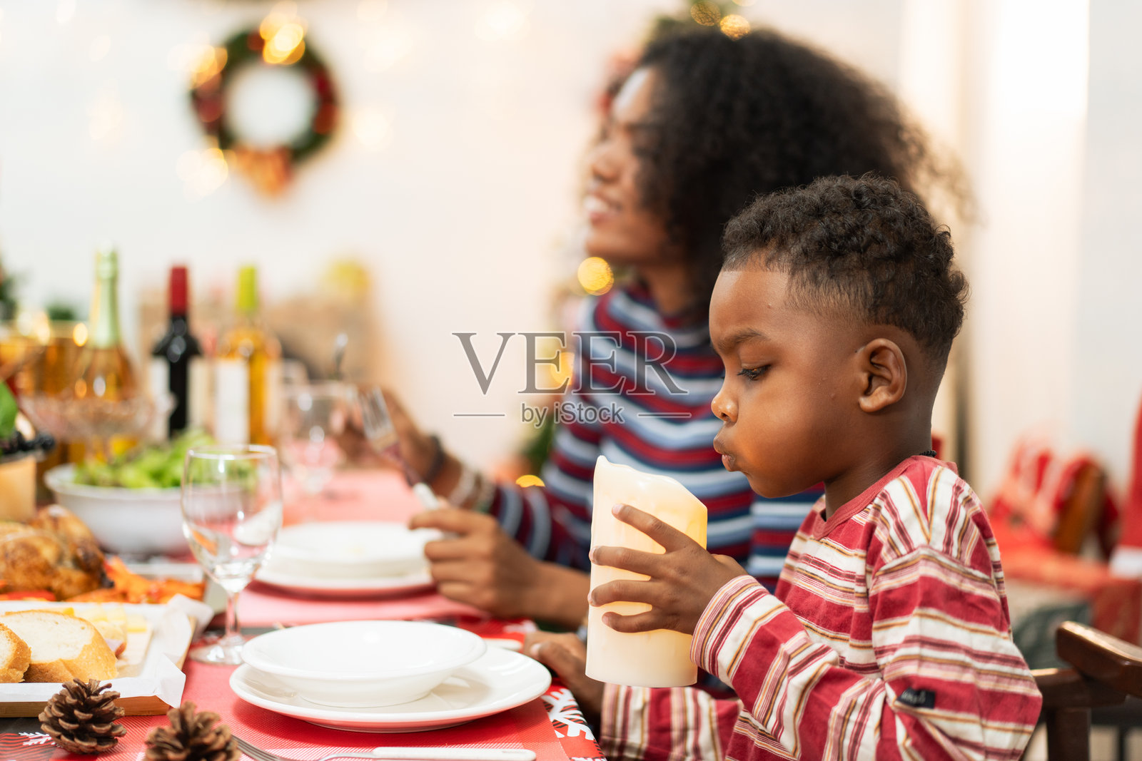 非洲男孩在圣诞节家庭晚餐时，顽皮地吹灭装饰蜡烛，大家一起享受圣诞派对的欢乐。照片摄影图片