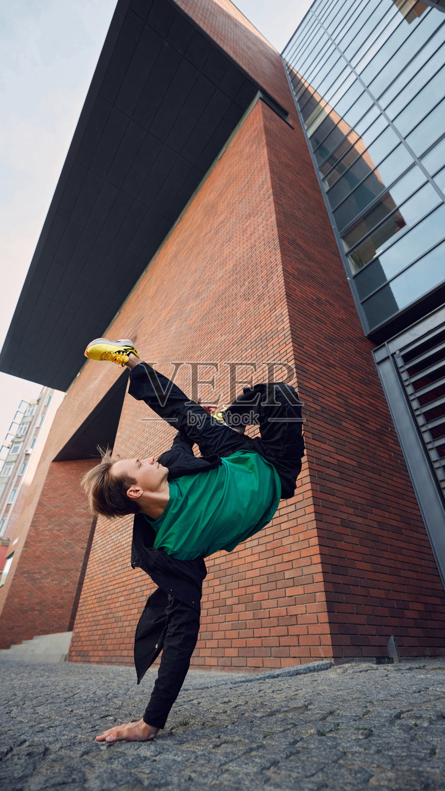街头舞者穿着时尚服装，在现代建筑的背景下表演令人惊叹的倒立翻转。照片摄影图片
