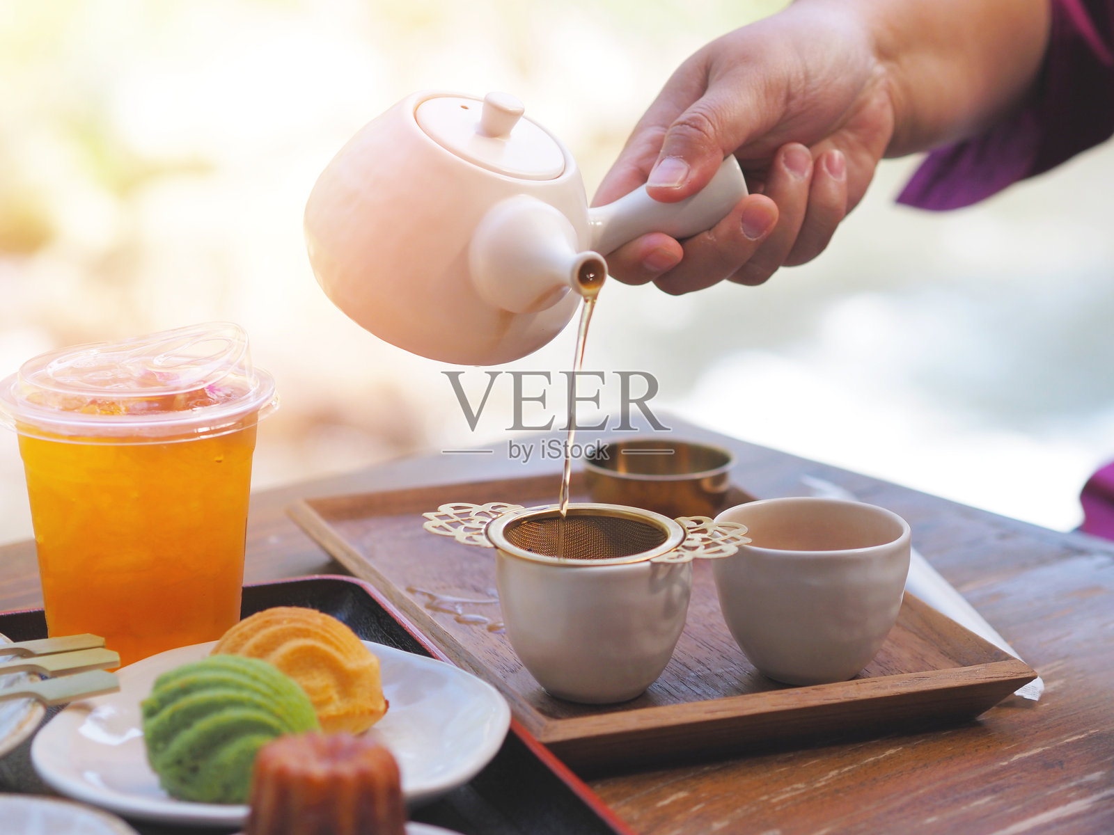 手握茶壶，将热茶通过过滤器倒入杯中照片摄影图片
