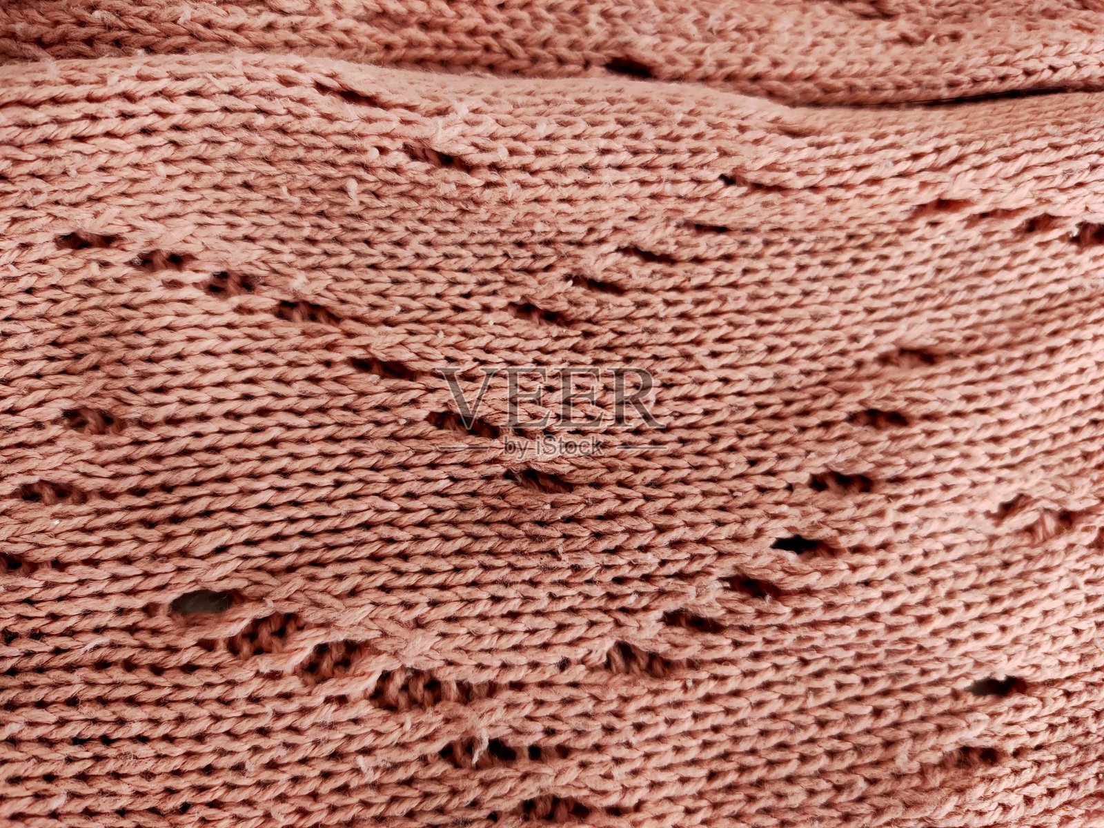 特写的有纹理的尘玫瑰色针织面料，带有孔眼针织图案。照片摄影图片