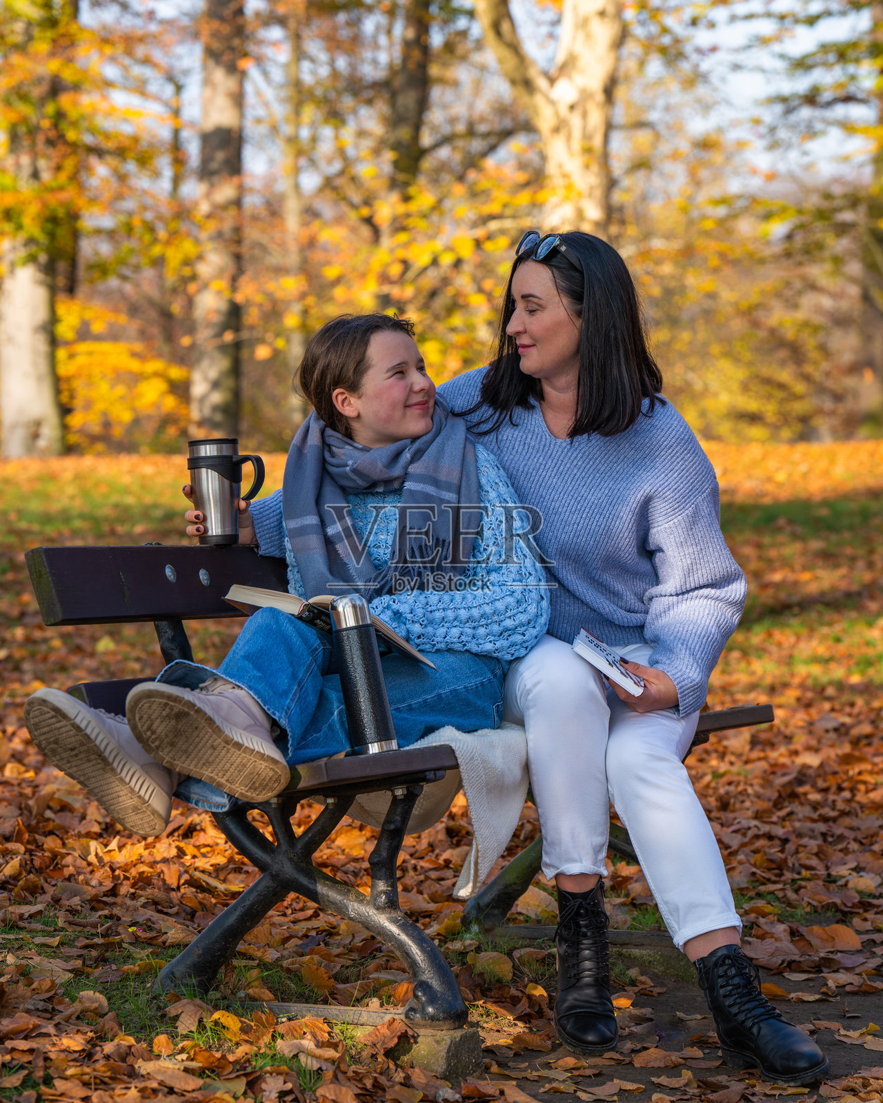 快乐的妈妈和青少年女儿坐在秋天公园的长椅上，阅读一本书。家庭亲密，团聚，家庭。照片摄影图片