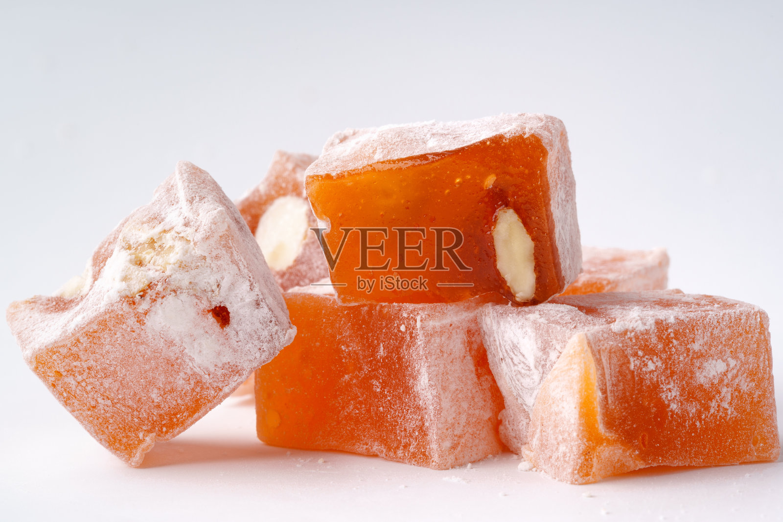 美味的橙色土耳其软糖方块，配有坚果，撒上糖粉，背景为浅色。照片摄影图片