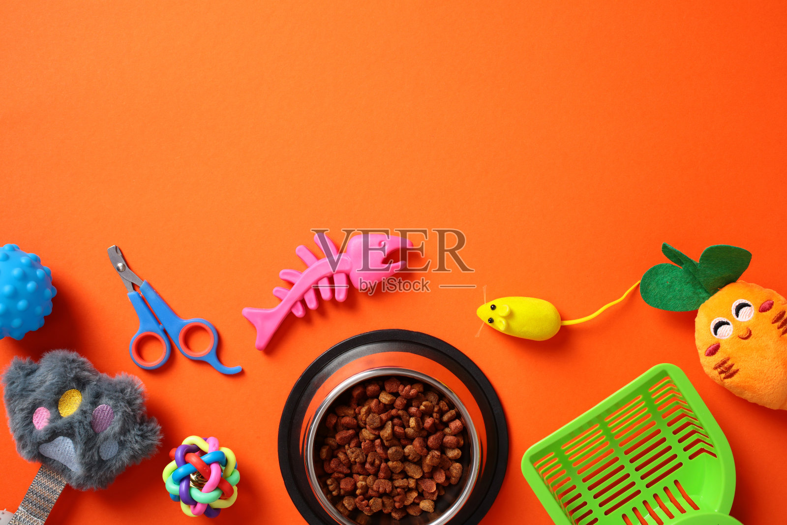五颜六色的猫玩具和配件在橙色背景上生动展示，包括一个食碗、修剪剪刀，以及像老鼠玩具和鱼骨玩具这样的玩乐物品。宠物护理概念照片摄影图片