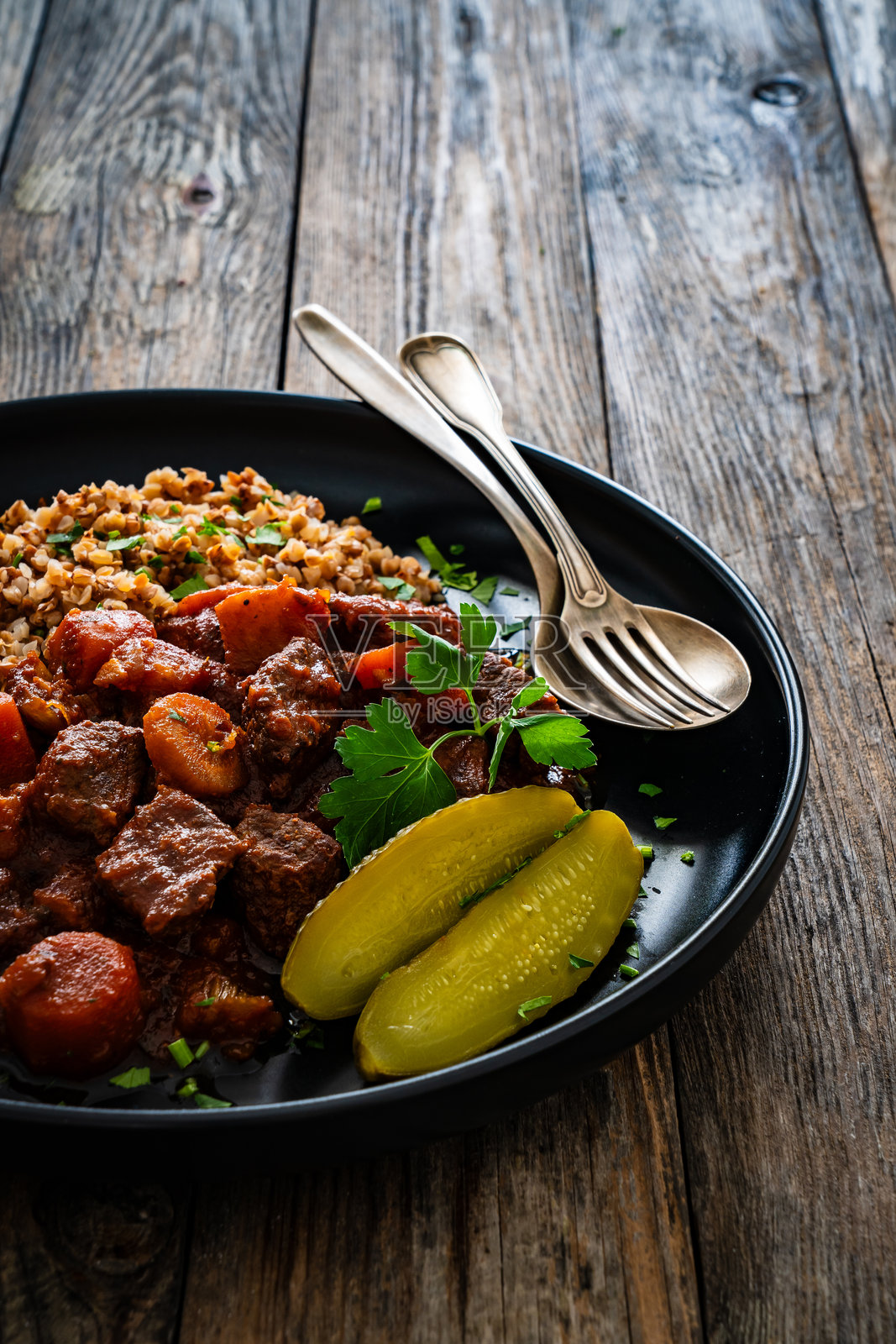 牛肉炖菜配荞麦粒和酸黄瓜，摆放在木桌上照片摄影图片