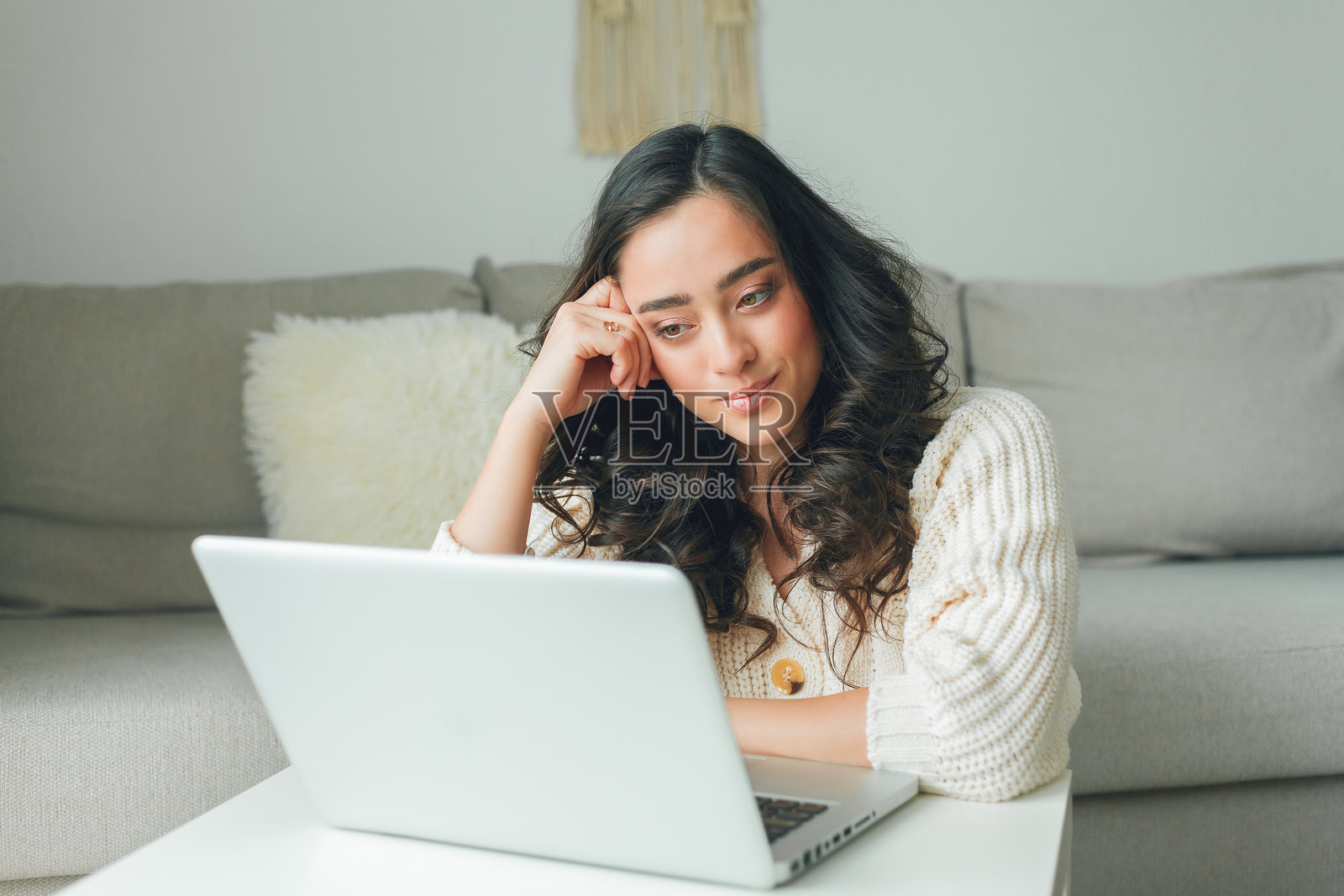 年轻的黑发女性在家中办公室使用笔记本电脑工作。美丽的模特穿着针织毛衣，环境温馨。自由职业者。照片摄影图片