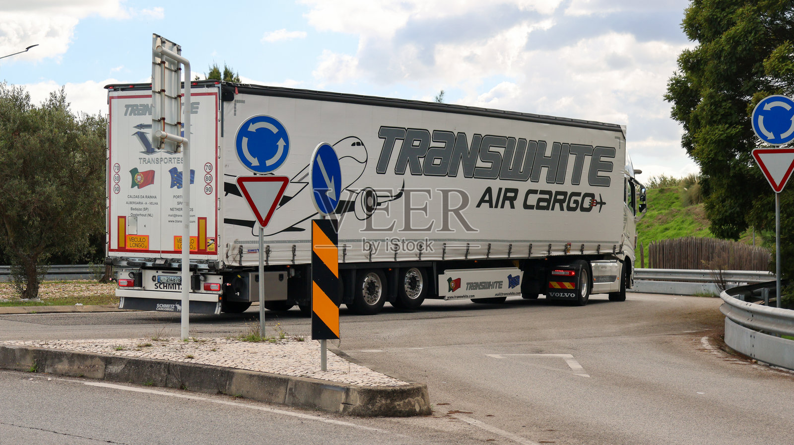 白色沃尔沃卡车在阳光明媚的日子里驶出环形交叉口，运输货物。照片摄影图片