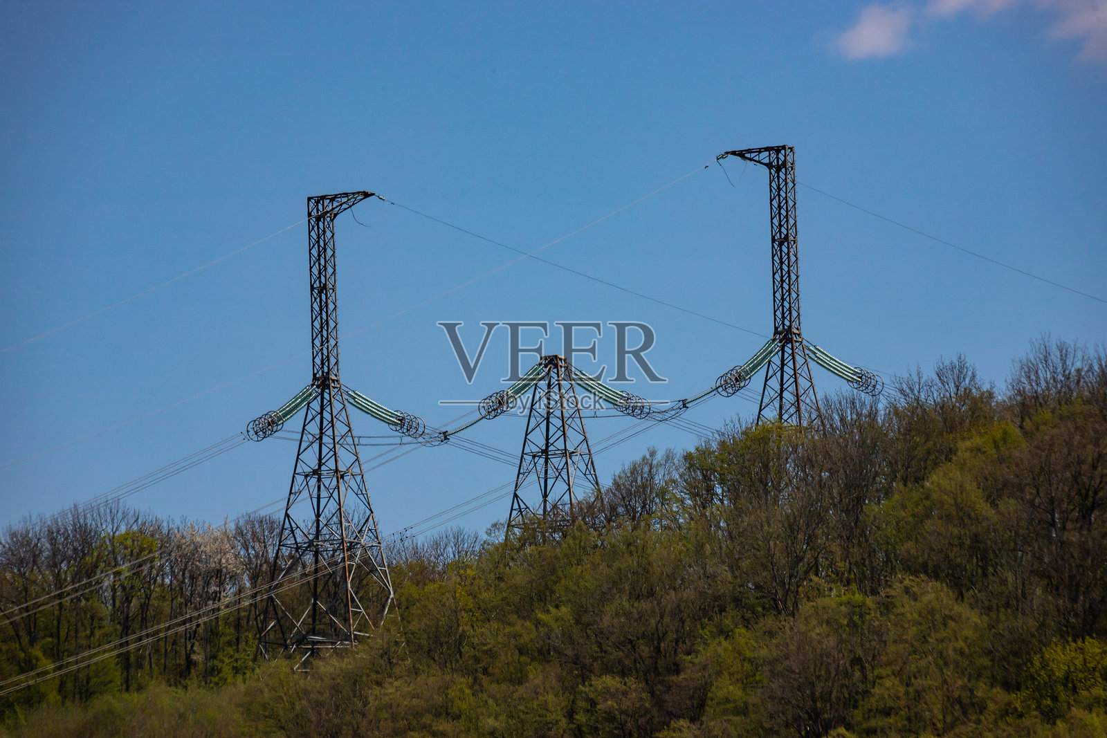 电力传输塔在阳光明媚的白天矗立在绿丘之上，背景是湛蓝的天空。照片摄影图片