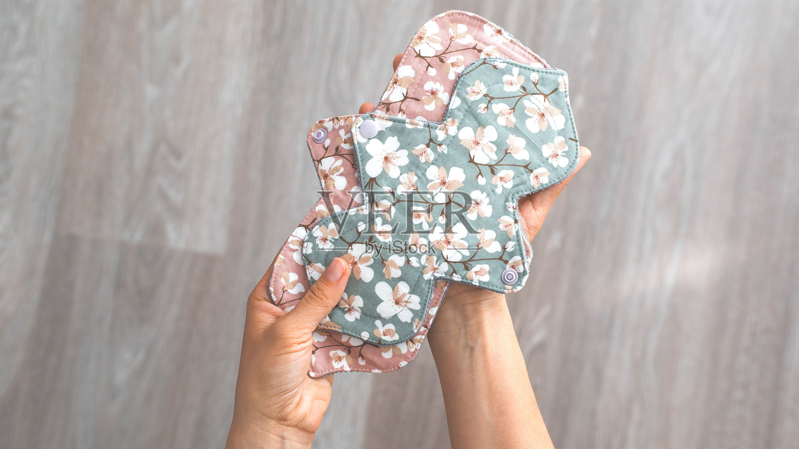 手握着带有花卉图案的可重复使用布质月经垫，色彩柔和，展示环保和可持续的生理期护理选择，木质背景，月经概念照片摄影图片