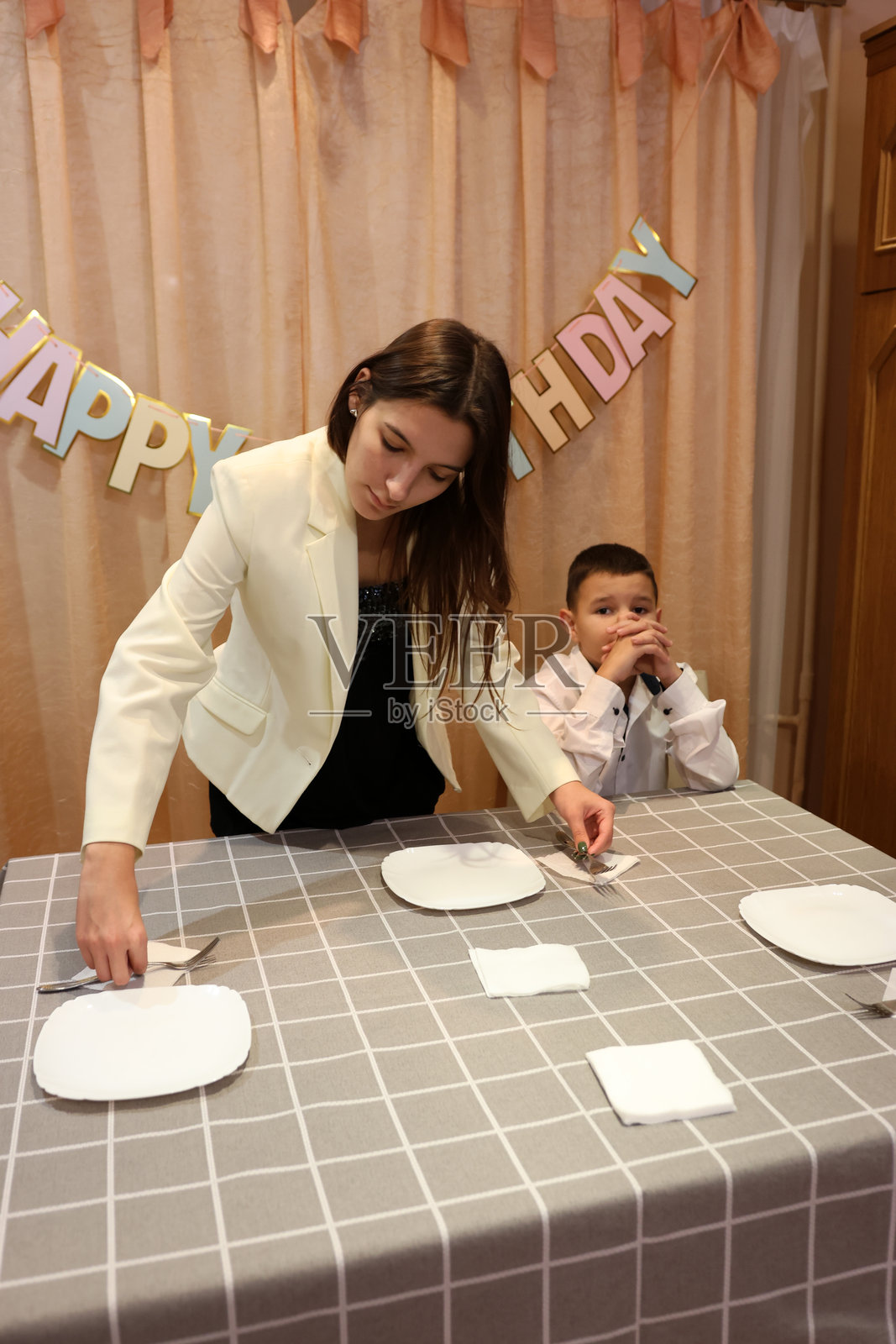 一个女孩和她的弟弟为生日庆祝活动装饰房间和节日餐桌。柔和的灯光。照片摄影图片