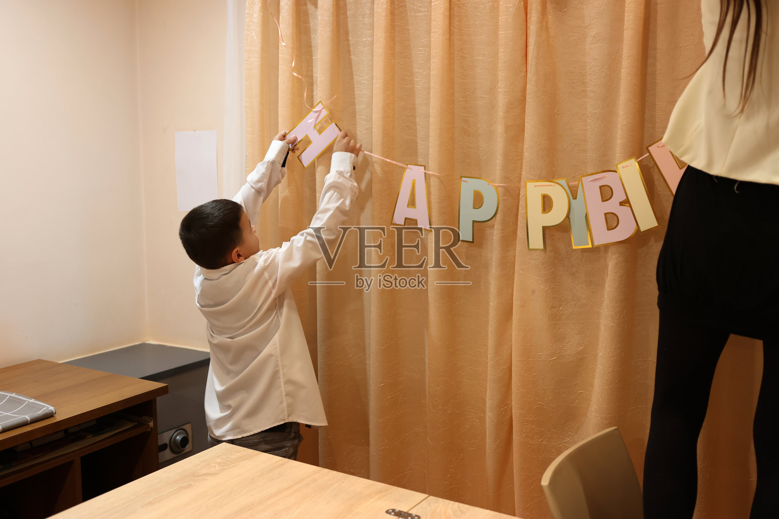 一个女孩和她的弟弟为生日庆祝活动装饰房间和节日餐桌。柔和的灯光。照片摄影图片