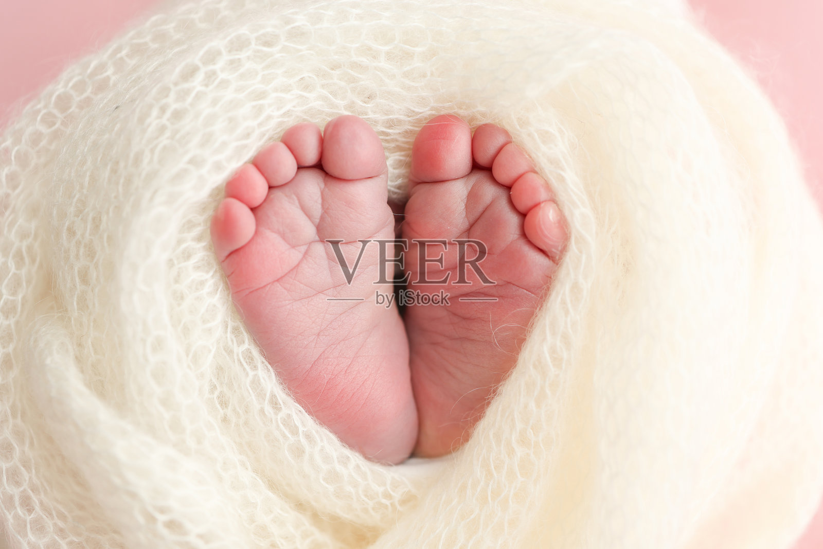 新生儿的小脚。新生儿柔软的脚在白色羊毛毯子上，粉色背景。特写新生儿的脚趾、脚跟和脚。工作室微距摄影。女性的幸福。照片摄影图片