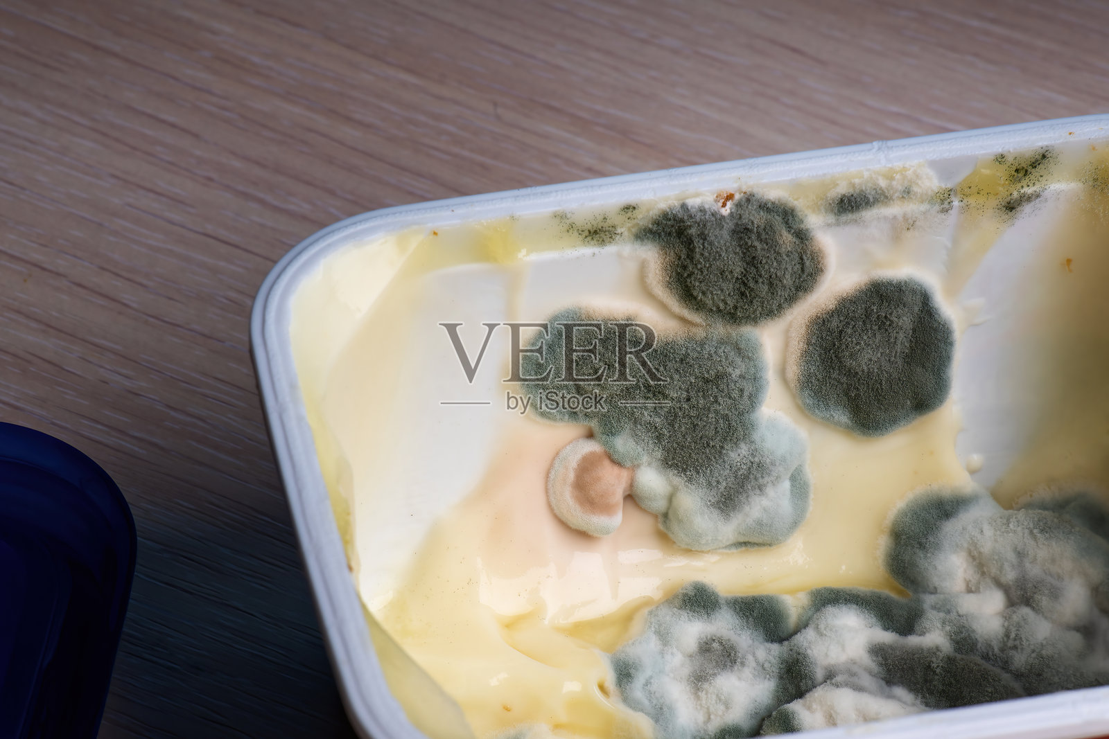 一罐融化的奶酪显示出明显的霉菌和真菌迹象，表明其已经变质。该图像突显了食品安全和正确储存实践的重要性。照片摄影图片