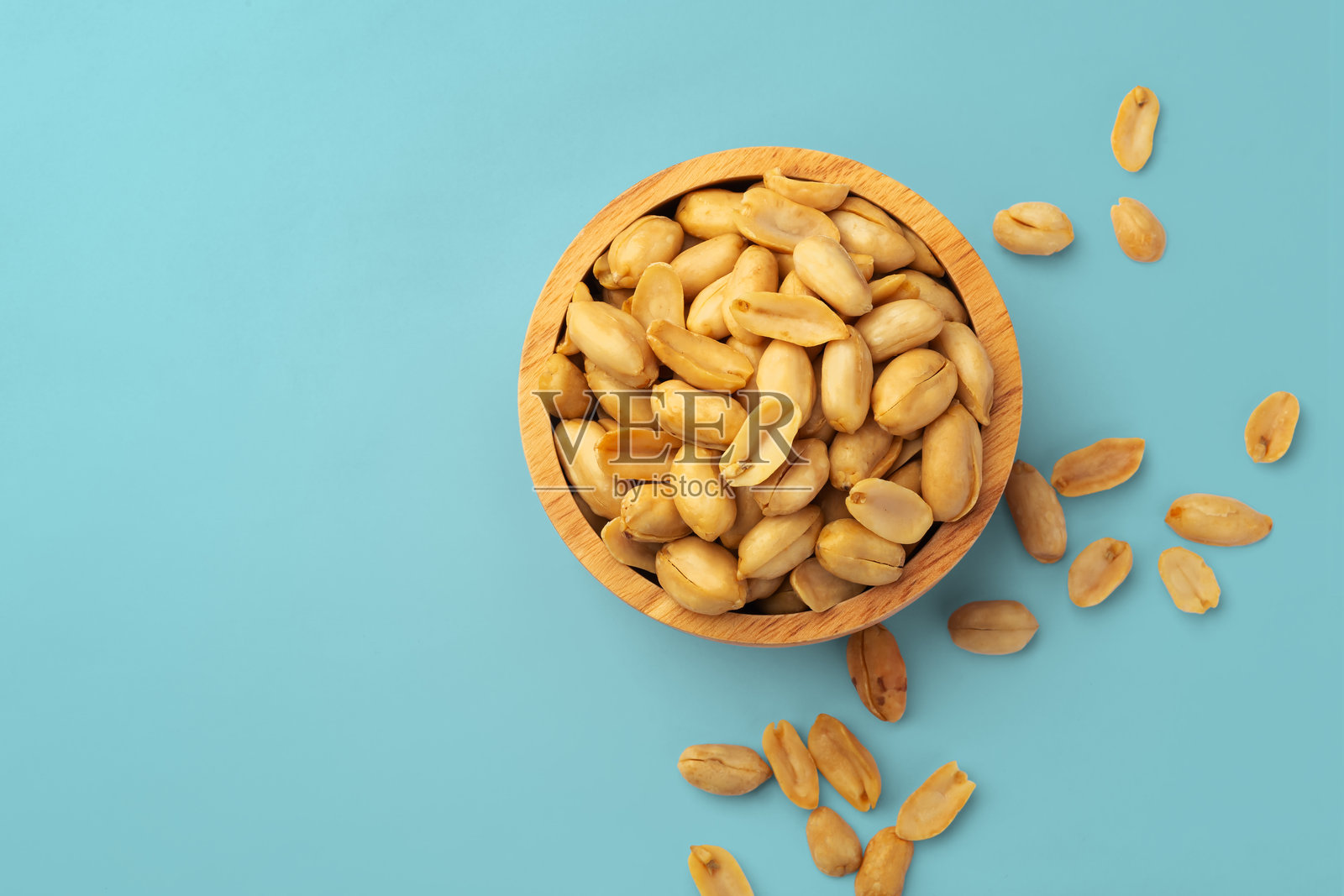 蓝色背景上的木碗里盛着烤花生，俯视图照片摄影图片