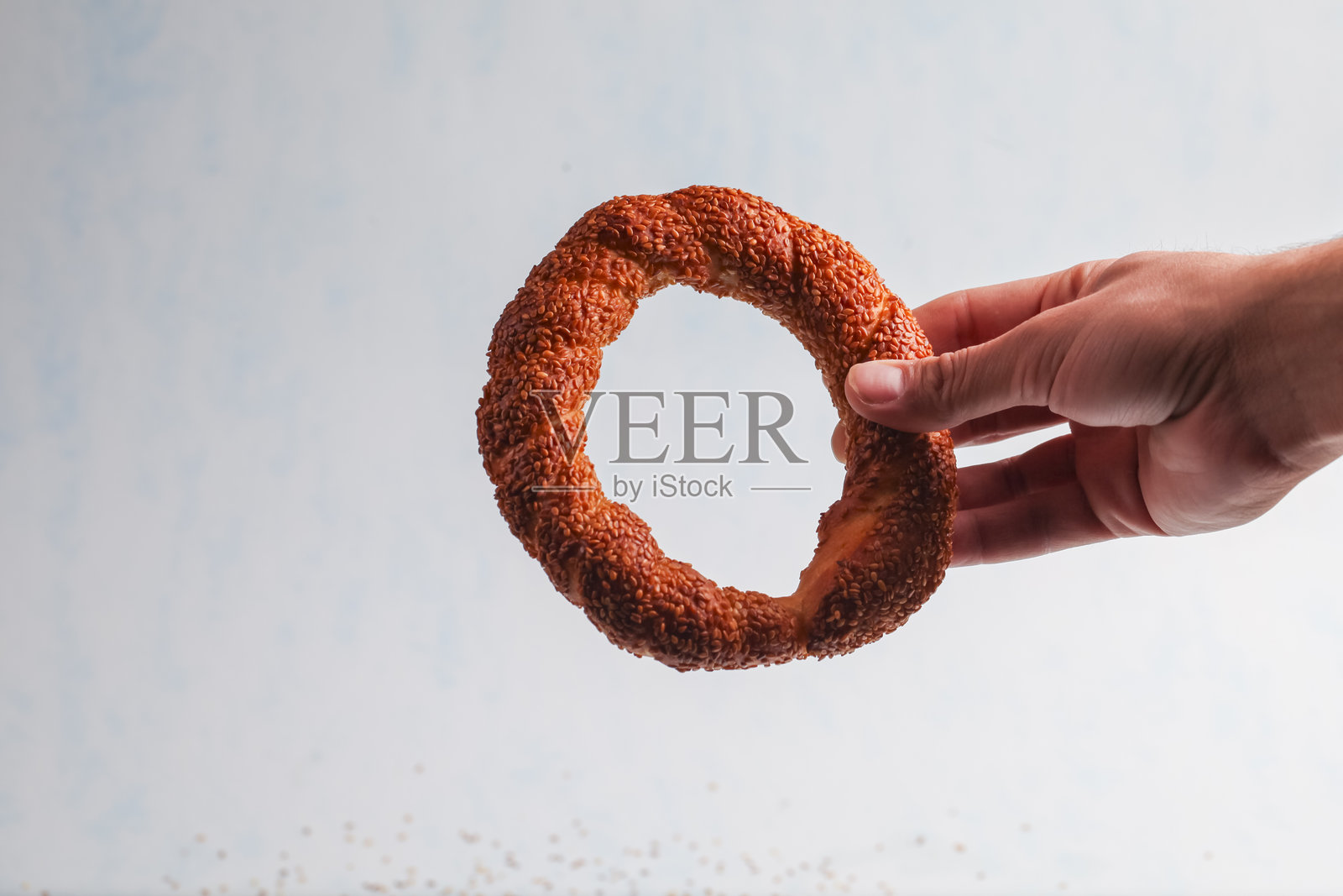 手持独特的芝麻圈面包，背景明亮照片摄影图片