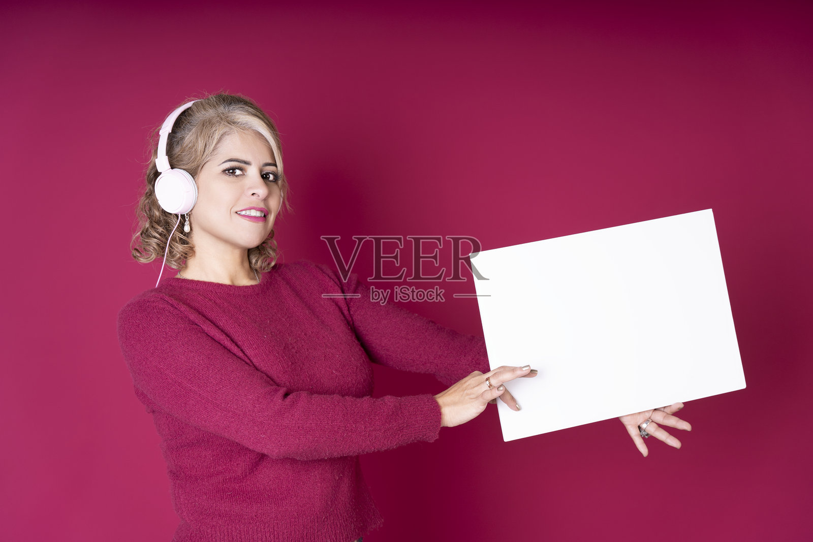 微笑的女性戴着耳机，展示空白白板，同时在听音乐照片摄影图片