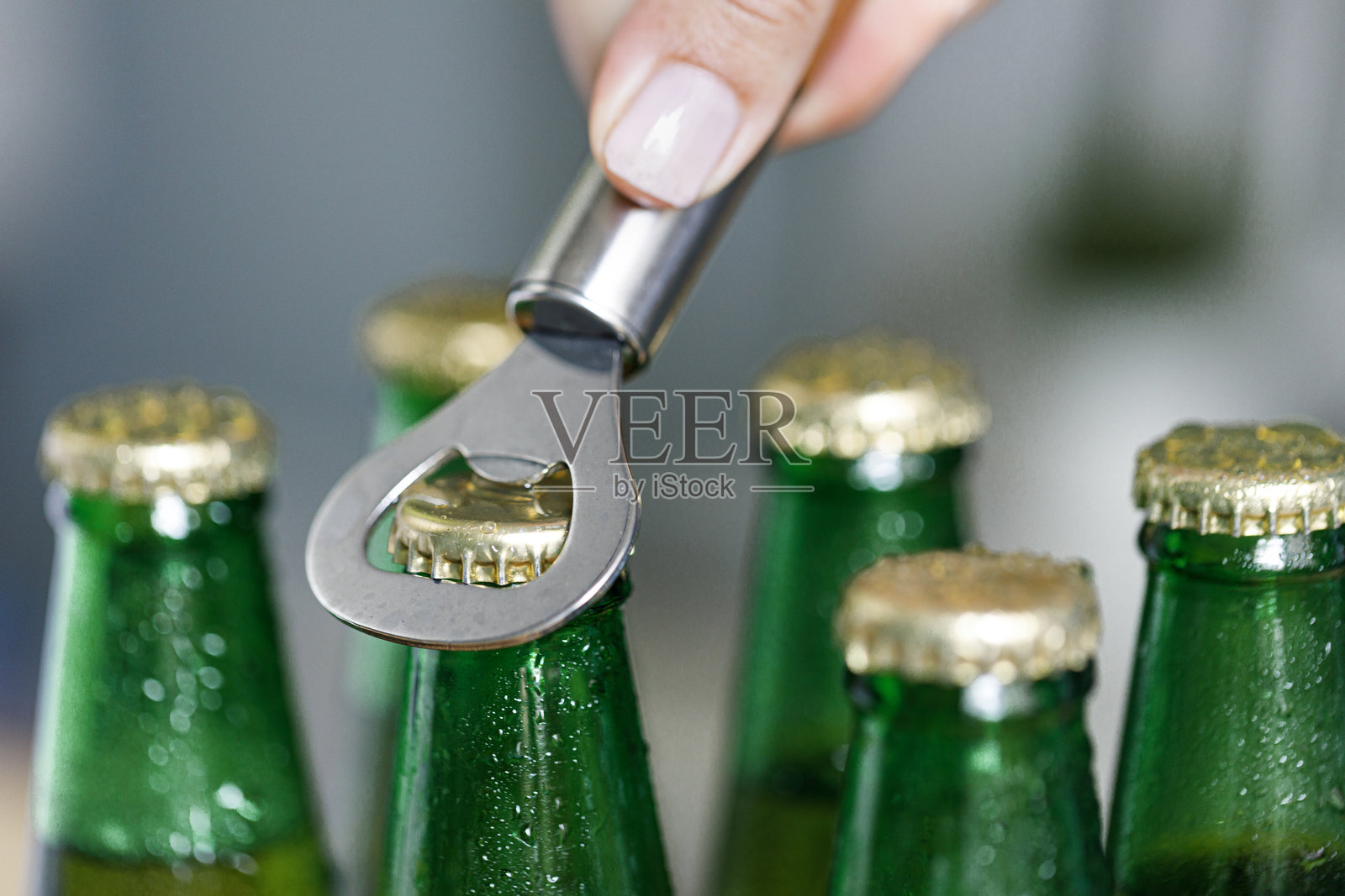 女性手用金属开瓶器打开啤酒瓶照片摄影图片