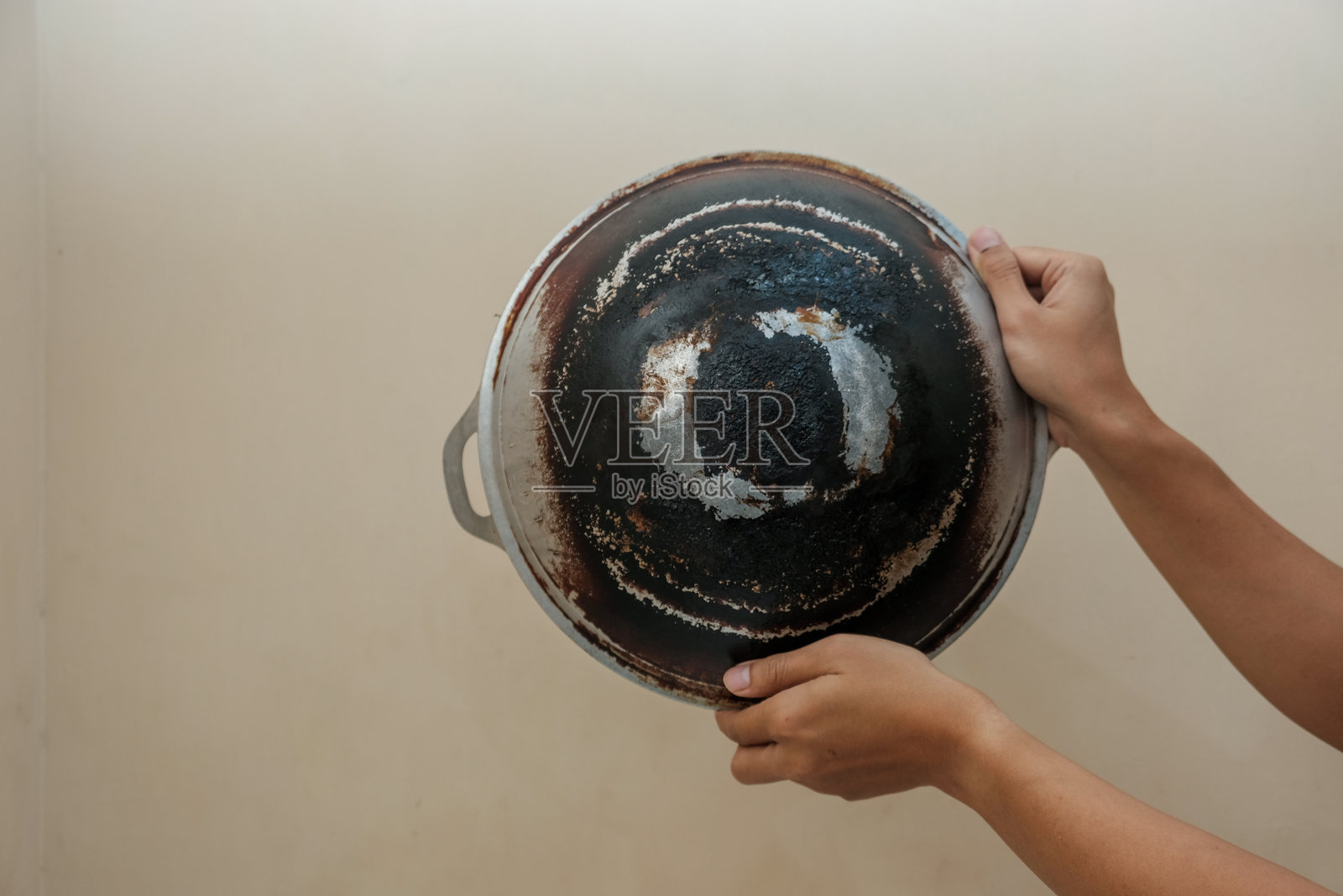 男人手握平底锅的特写，焦黑的平底锅背面在奶油色背景上。照片摄影图片