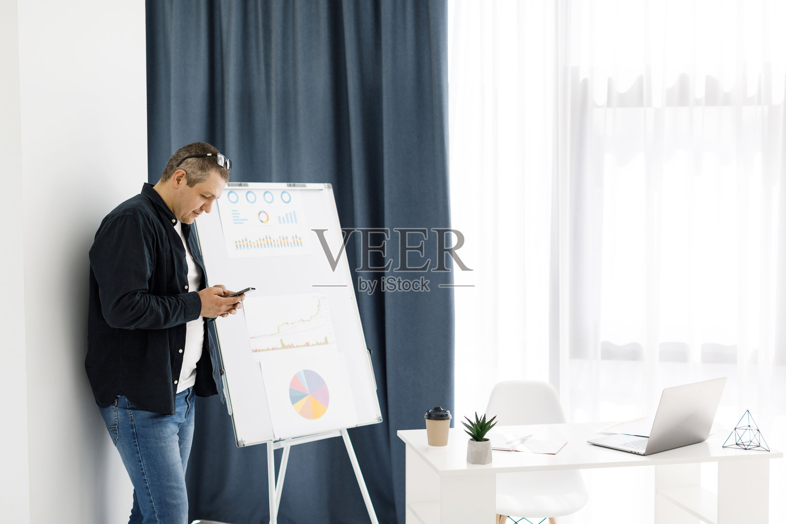 一名穿着休闲服的男子在办公室工作，手里拿着手机。照片摄影图片