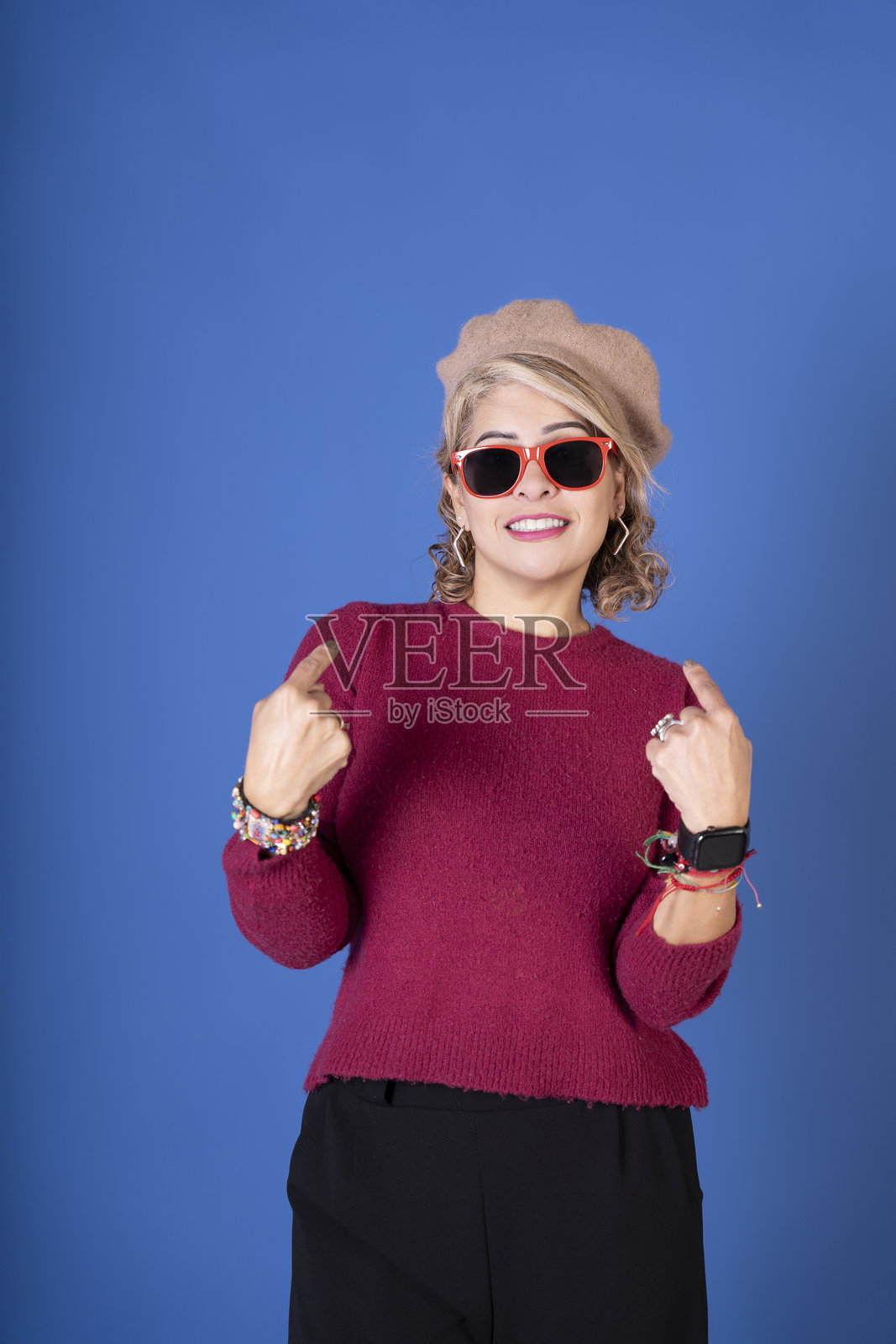 微笑的女性用双手食指指向下方，背景为蓝色照片摄影图片