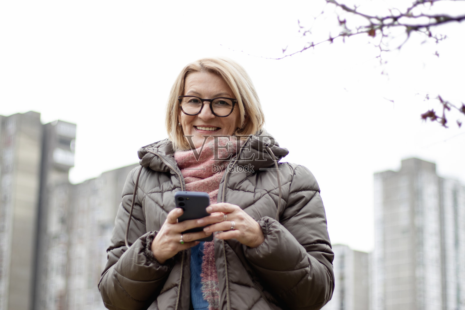戴着眼镜的成熟金发女性在冬日散步时享受使用手机的乐趣照片摄影图片