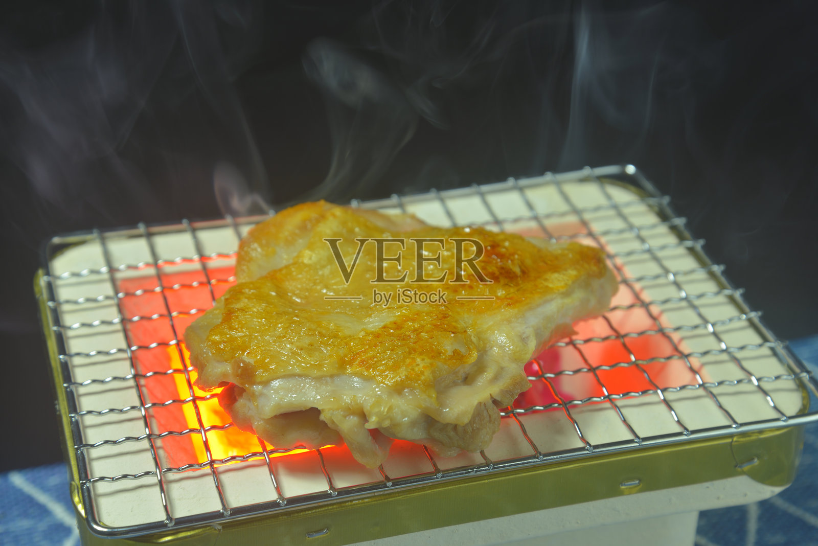 在炭火烤架上烤鸡腿，烟雾升起照片摄影图片