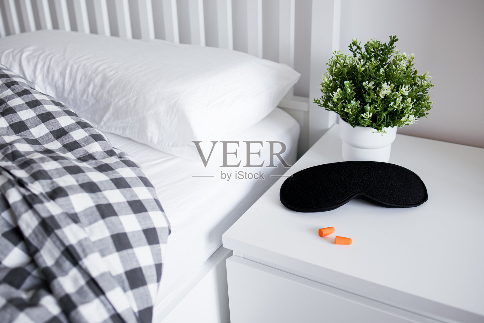 舒适的卧室布置，白色床头柜上放着睡眠眼罩、耳塞和植物照片摄影图片