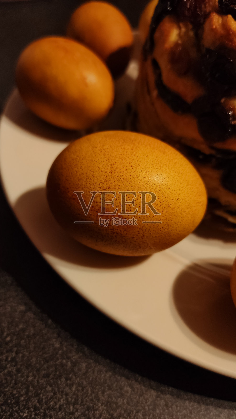 金色染色的洋葱复活节彩蛋摆放在白色盘子上，旁边是一块美味的库格尔霍夫蛋糕，营造出节日的复活节氛围。照片摄影图片