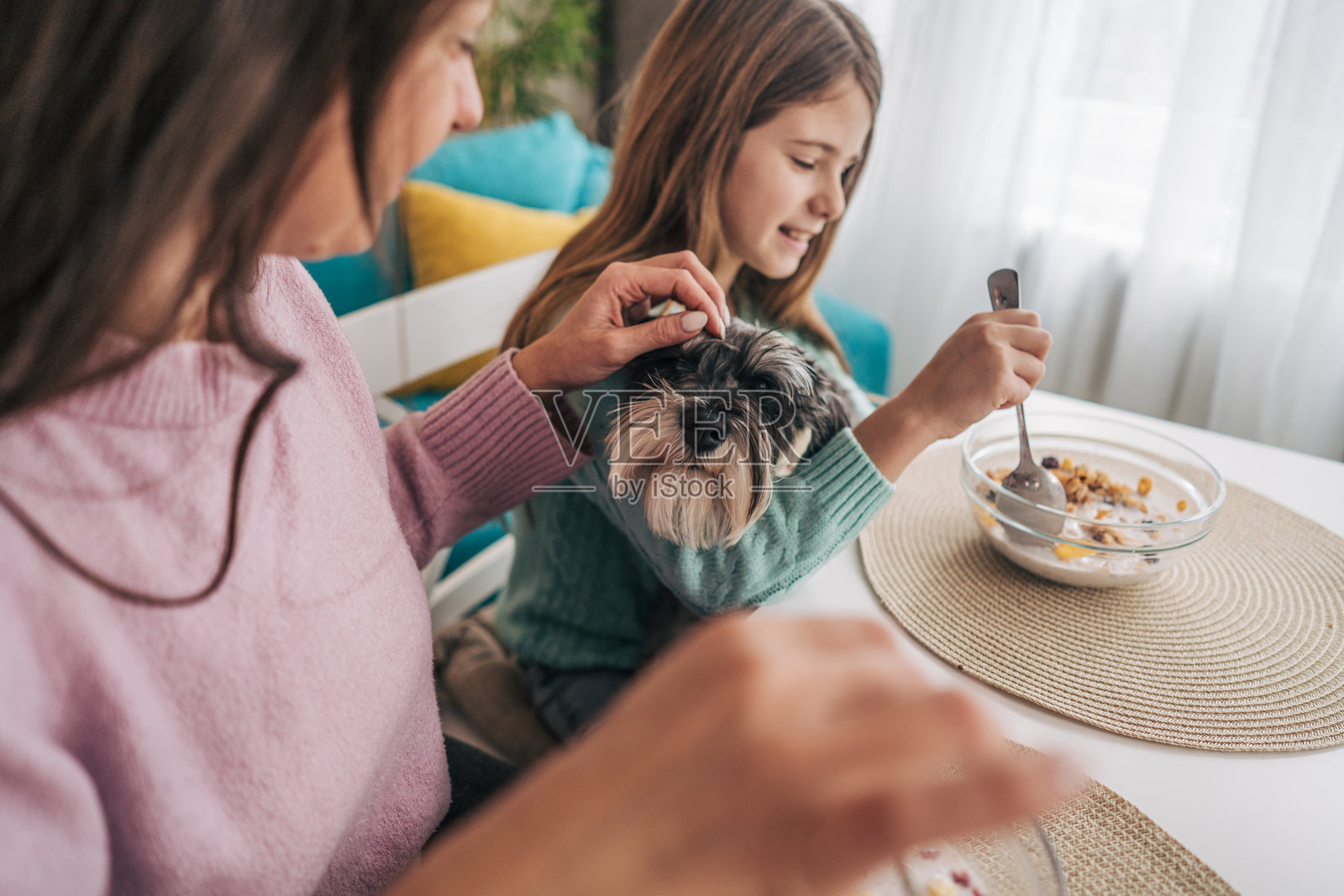 一位快乐的母亲和女儿坐在餐桌旁，一起享用早餐。她们在享受美食，晨光温柔地洒满房间。照片摄影图片
