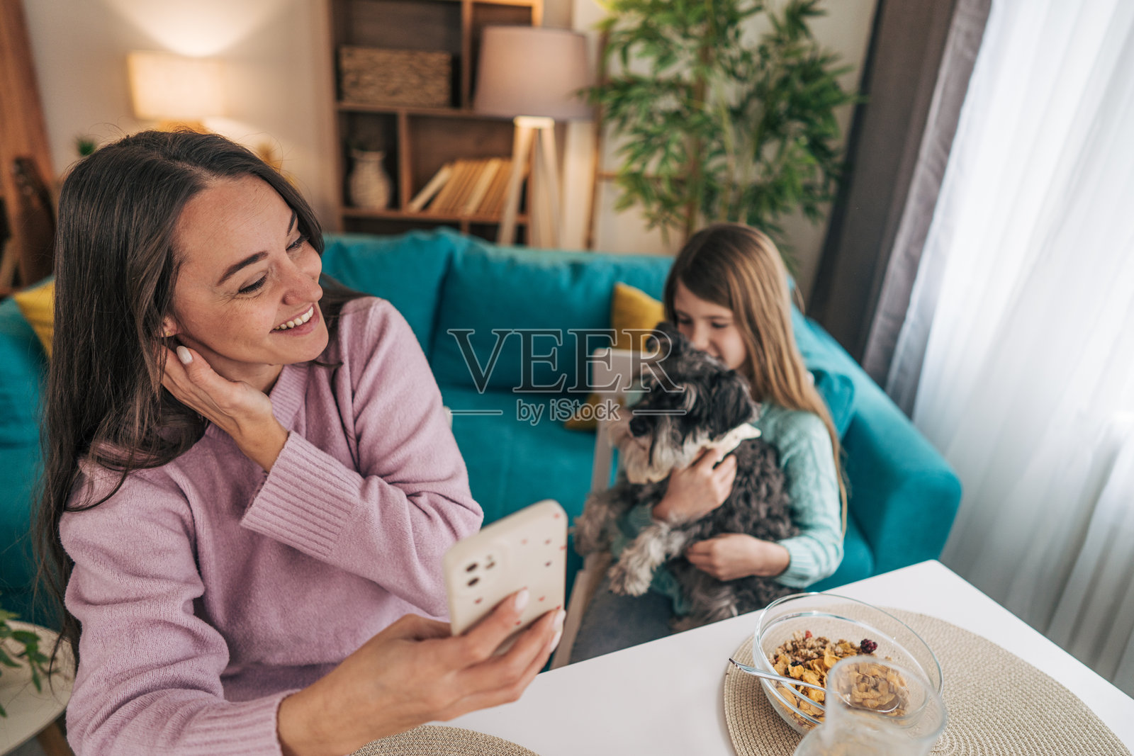 母亲坐着或站在附近，专注于手机，正在滚动或查看信息。她似乎沉浸在设备中，但仍然在这个空间中。照片摄影图片